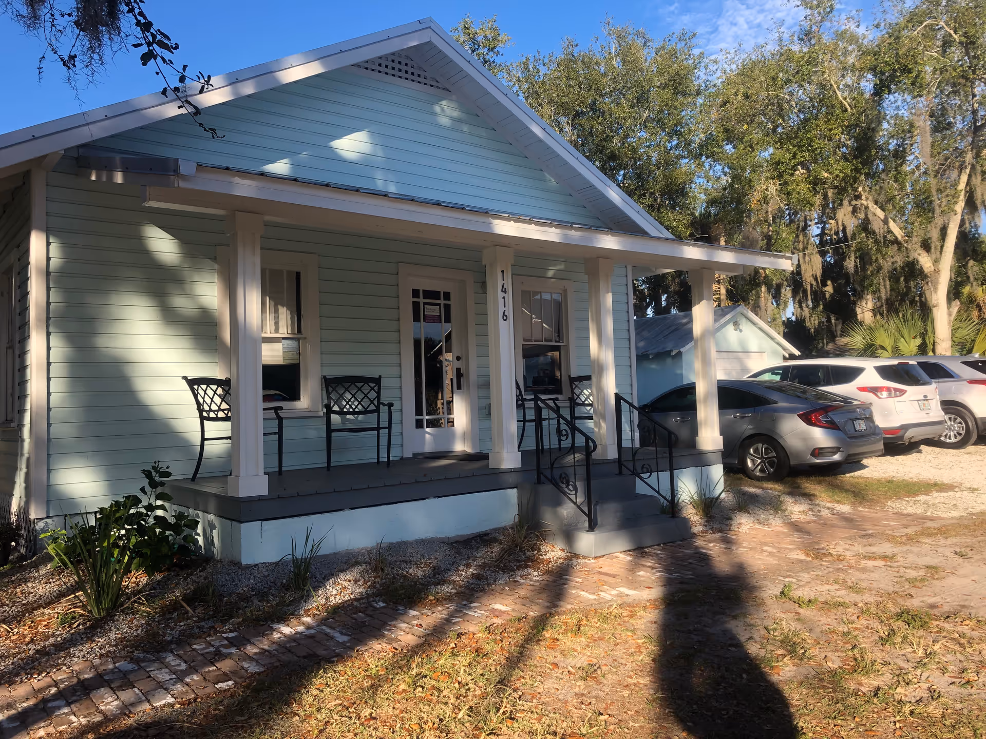 Light blue, single-story building with a covered porch and parked cars.