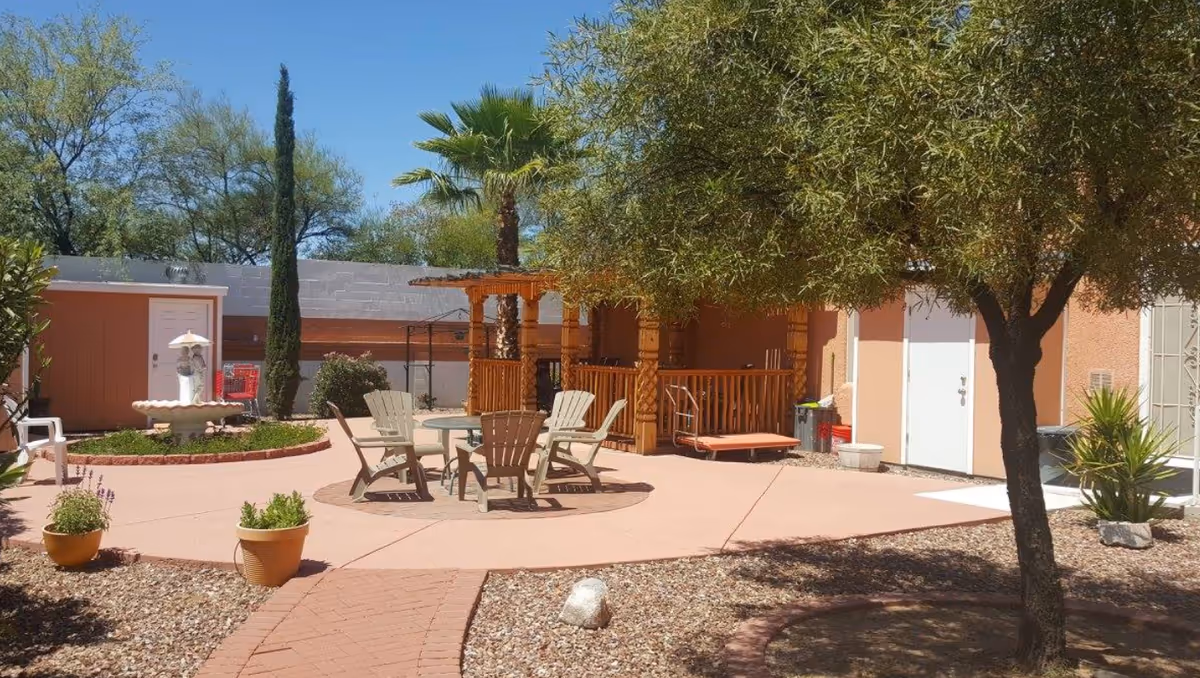 Outdoor courtyard with seating around a round table, a wooden pergola, plants, and a fountain.