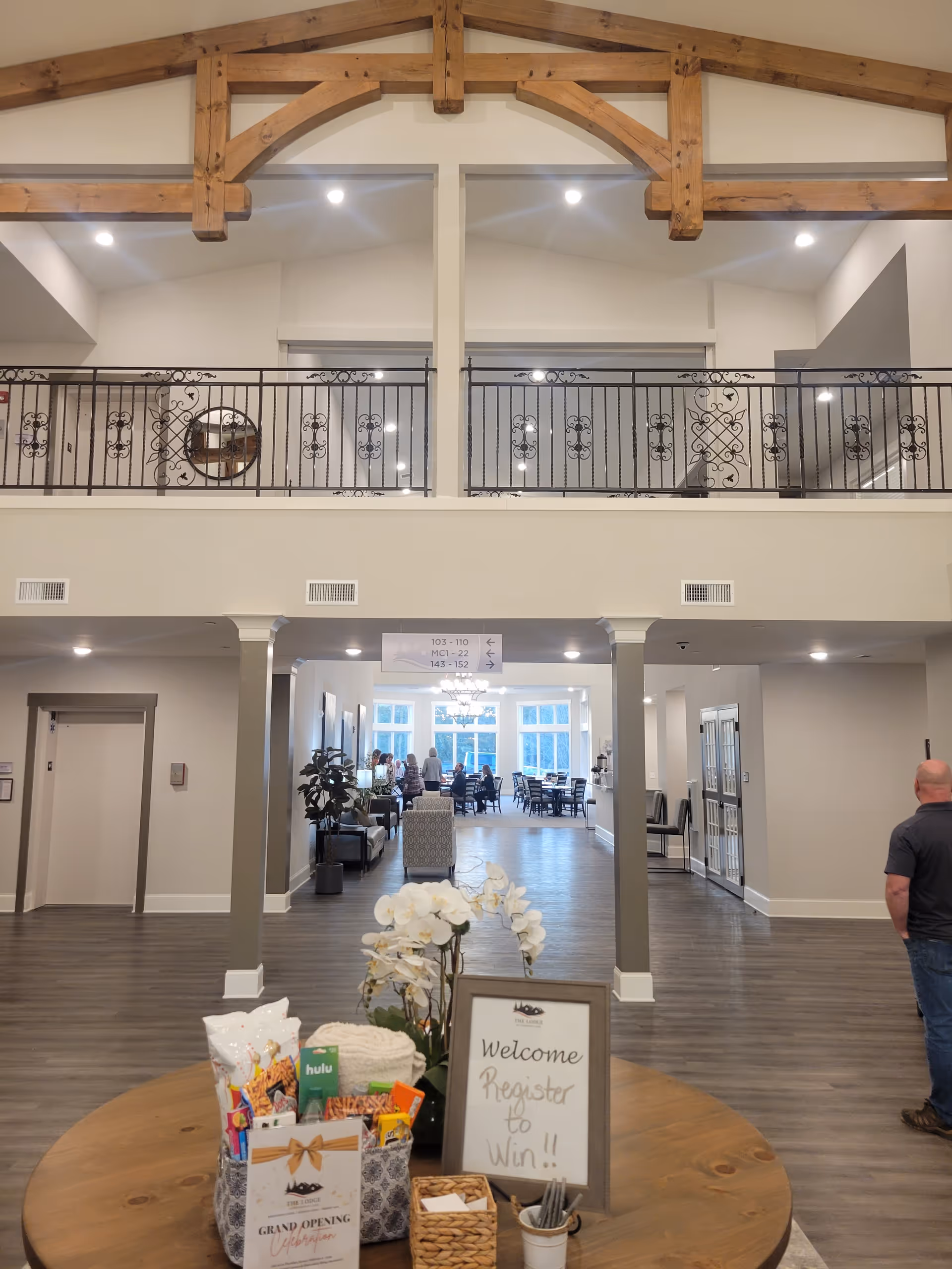 Spacious senior living lobby with wooden beams, railings, and a welcome table near a dining area.