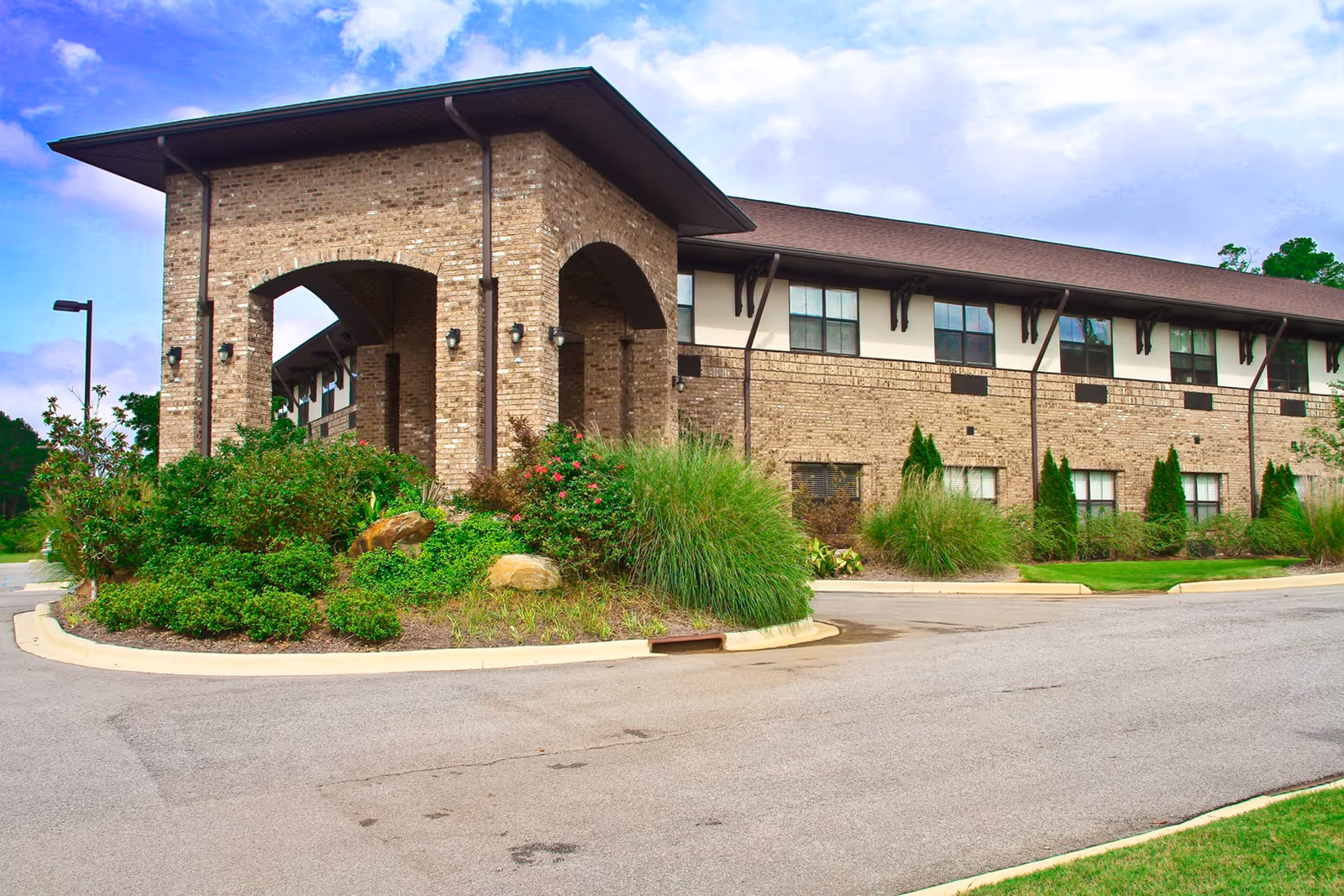 Brick senior living facility with arched entrance and manicured landscaping.
