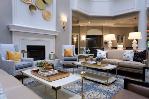 Bright, elegant common lounge with sofas and armchairs arranged around coffee tables in front of a fireplace and decorative wall art.