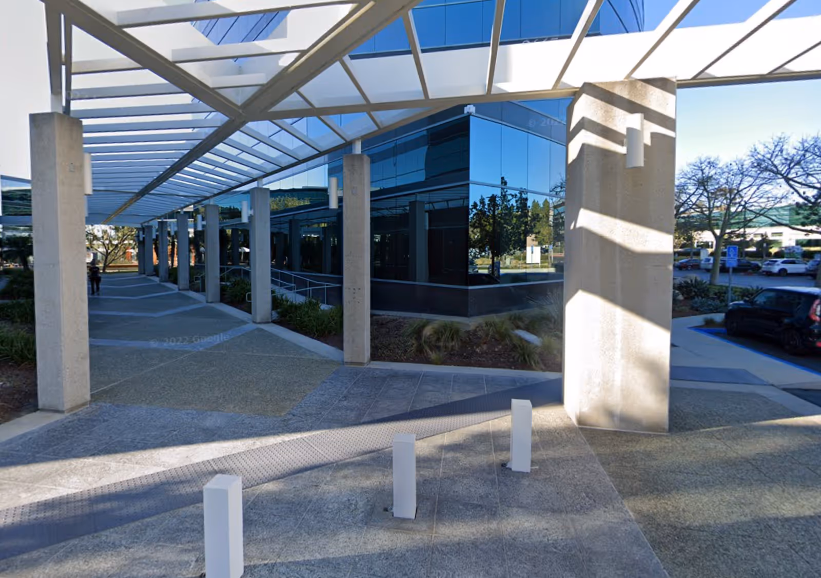 Modern building exterior with glass walls, tall concrete columns, and a covered walkway.