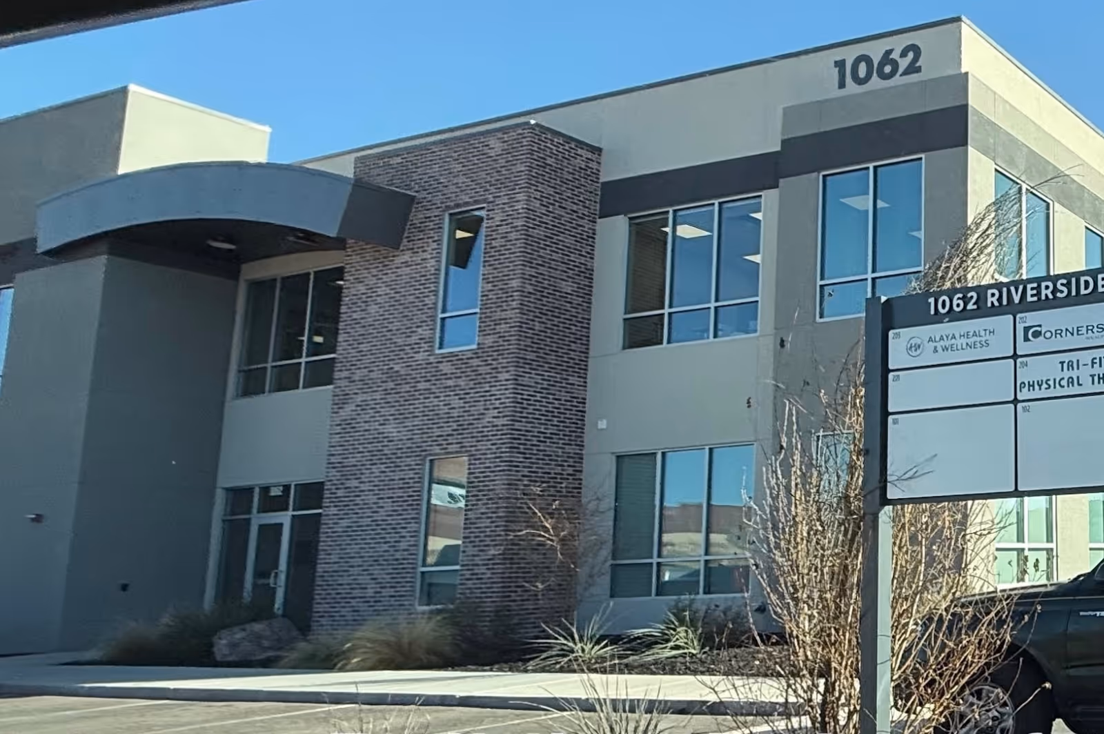 Exterior view of modern two-story medical building with brick column, large windows, and a street sign.
