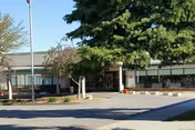 Exterior view of Medilodge of Sterling Heights with trees, entrance, and parking.