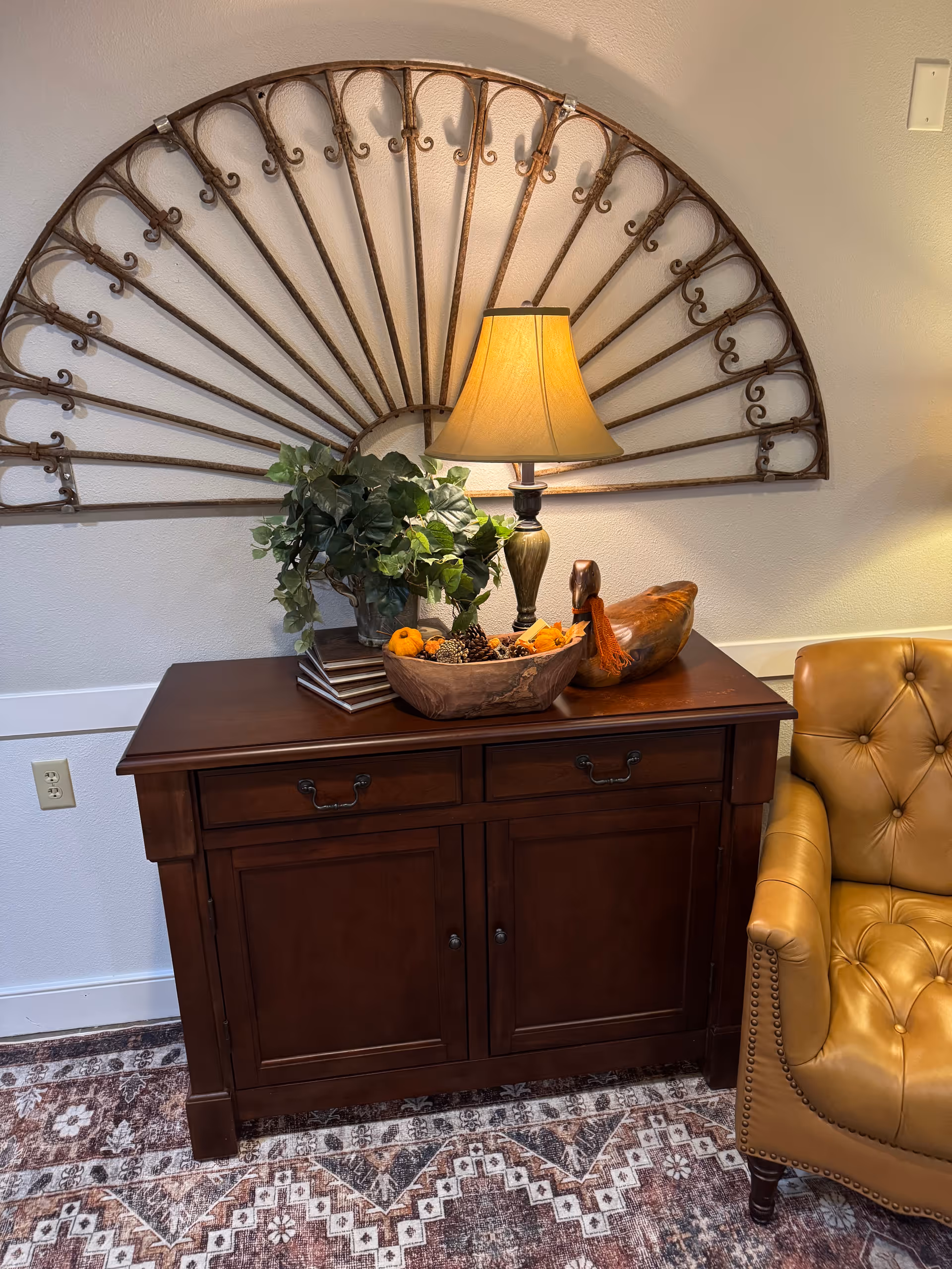 A wooden sideboard with a lamp, plant, and decorative bowl in a living room corner.