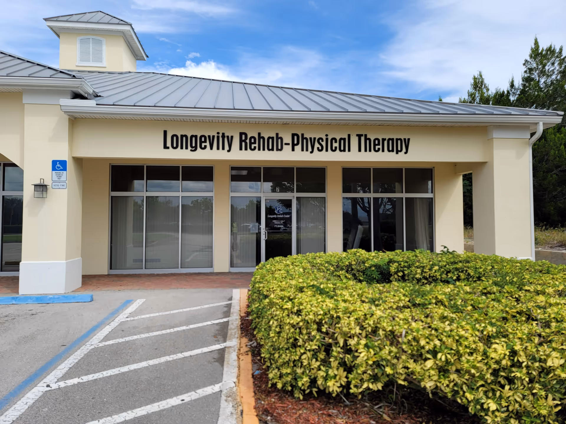 Front view of Longevity Rehab-Physical Therapy facility with glass doors and trimmed hedges.