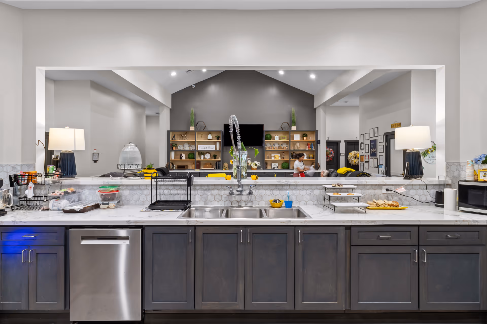 Modern kitchen counter with sink, appliances, and open view to a communal living area.