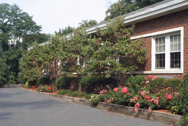 Brick building exterior of a senior living facility with windows and landscaped shrubs