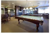 Lounge area with billiard tables, seating, and warm wood accents in a senior living facility.