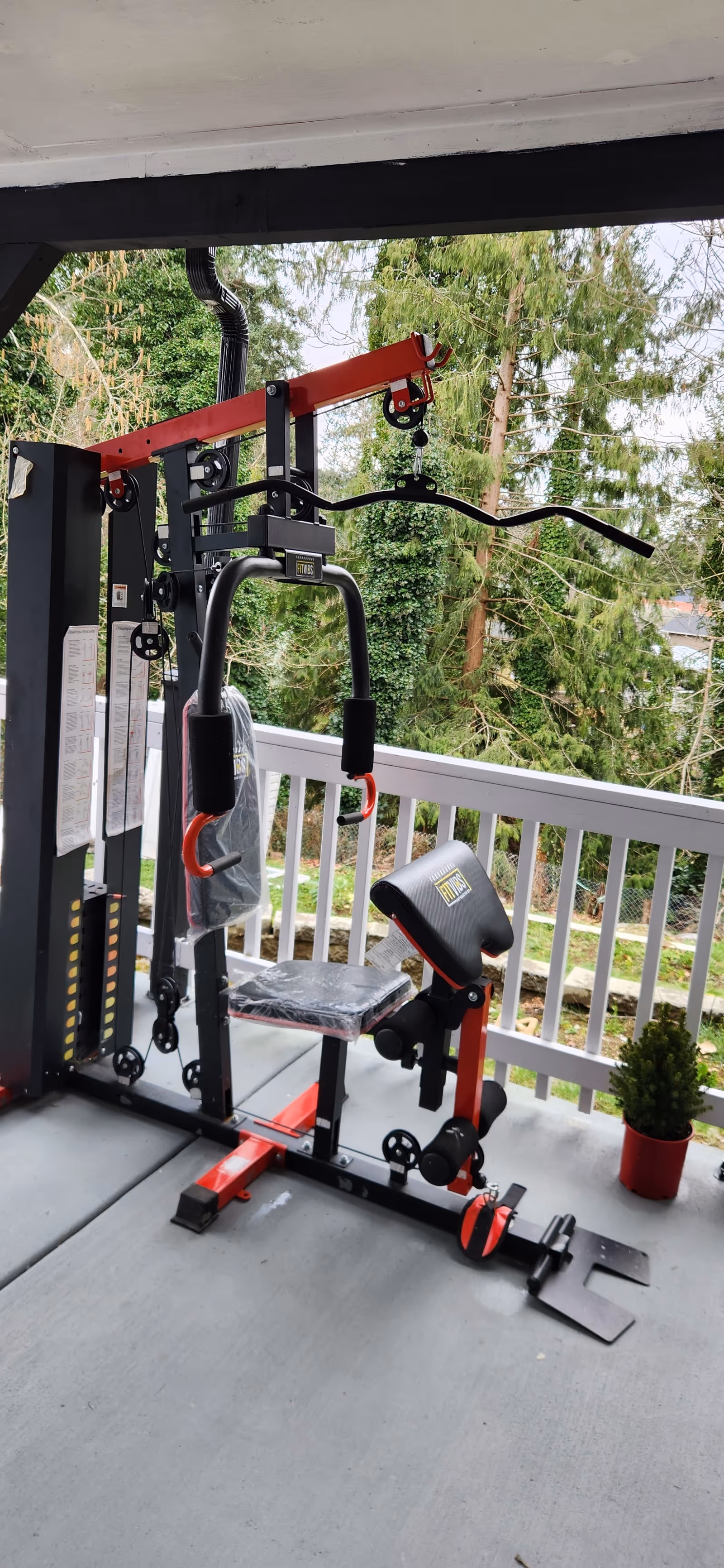 Outdoor balcony with fitness equipment, railing, a potted plant, and trees beyond.