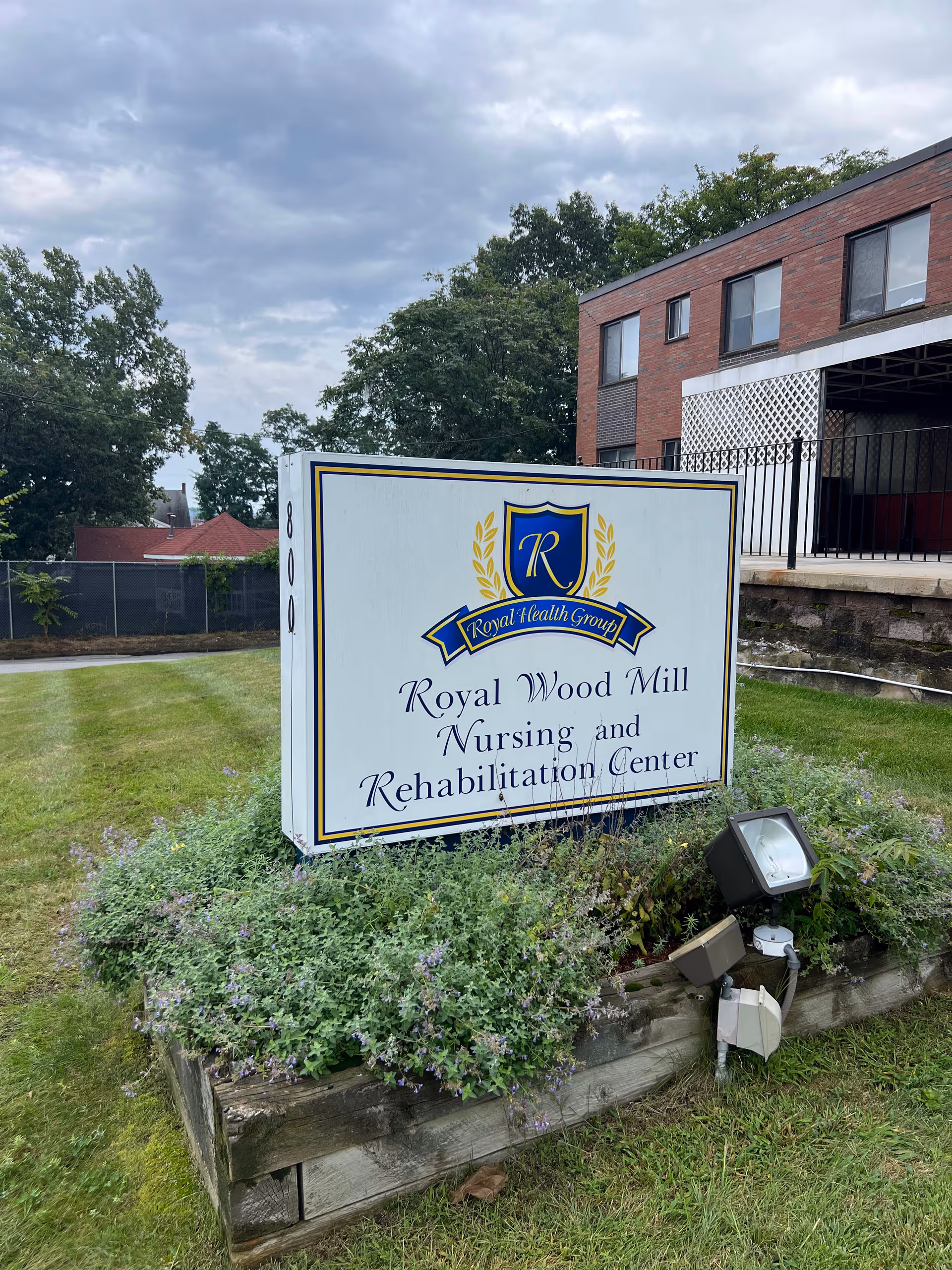 Exterior view of Royal Wood Mill Nursing and Rehabilitation Center sign with brick building behind.