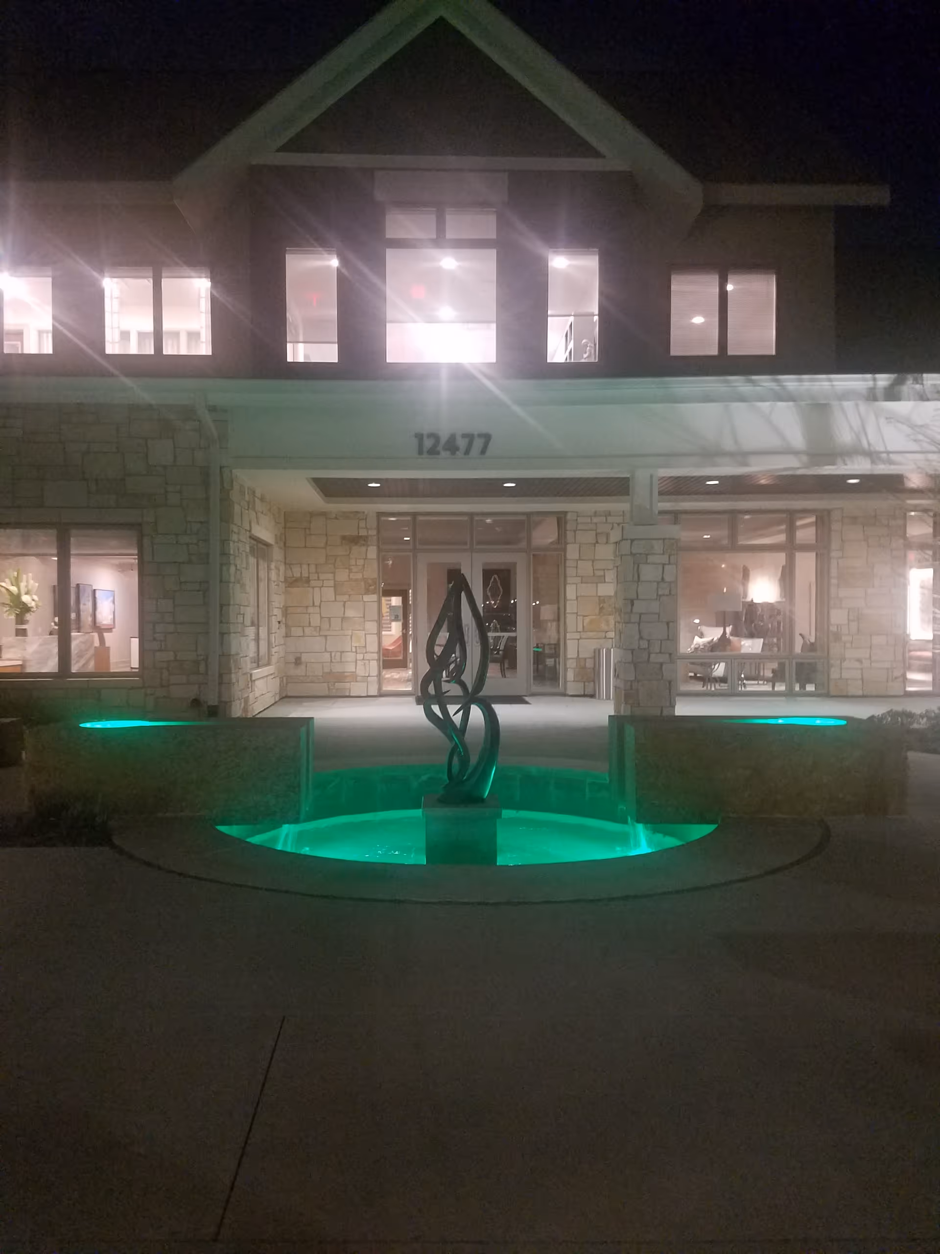 Night view of Faith Presbyterian Hospice entrance with an illuminated green fountain in front.