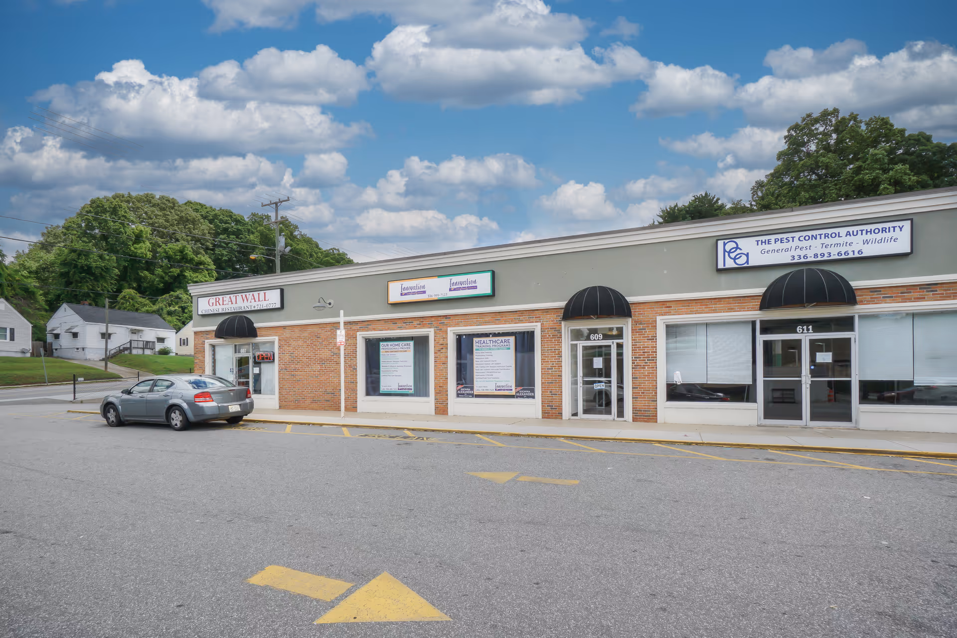 A brick storefront strip with multiple businesses along a parking lot and blue sky.