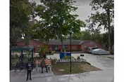 Exterior view of Arbor Village Inc facility with trees, a driveway, and people near a pavilion.