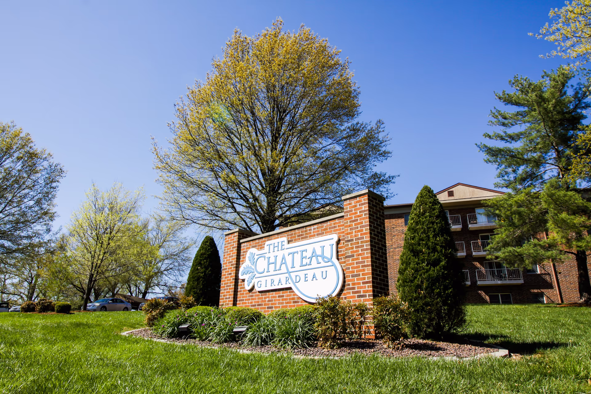 Brick building with a large sign reading The Chateau Girardeau, set among trees and green lawn.