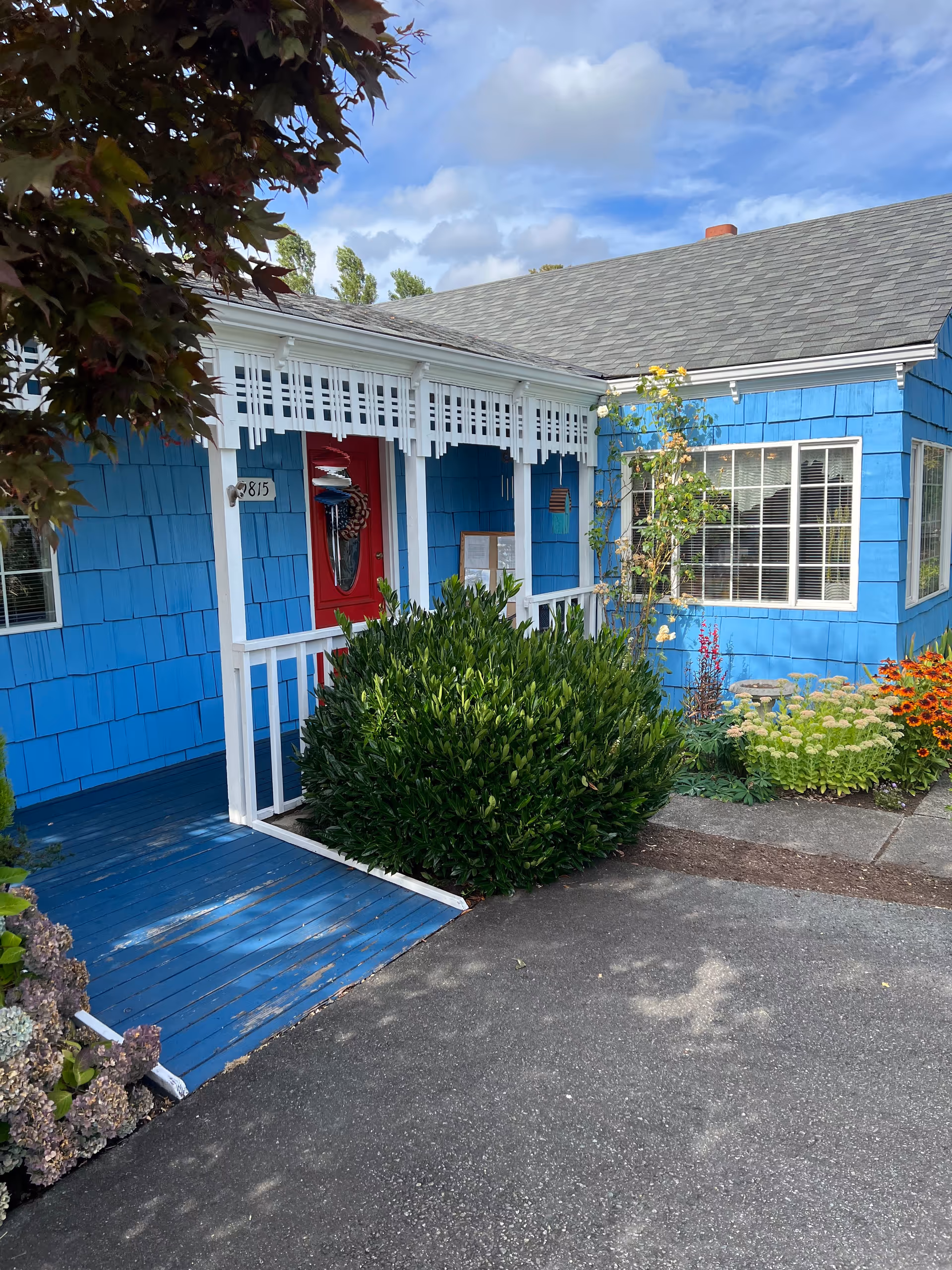 Bright blue senior-living frontage with white trim, red door, and landscaped entry walkway.