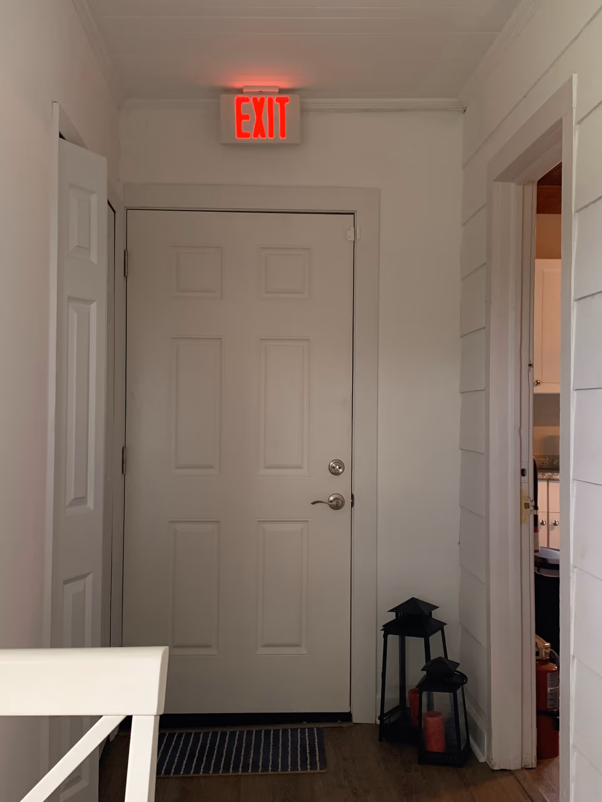 White interior hallway with an EXIT sign above a closed door and decorative lanterns.
