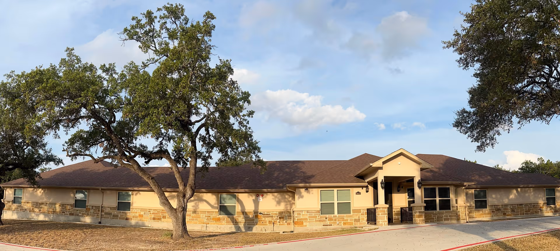 Single-story Timberwood Assisted Living building with stone accents and surrounding trees.