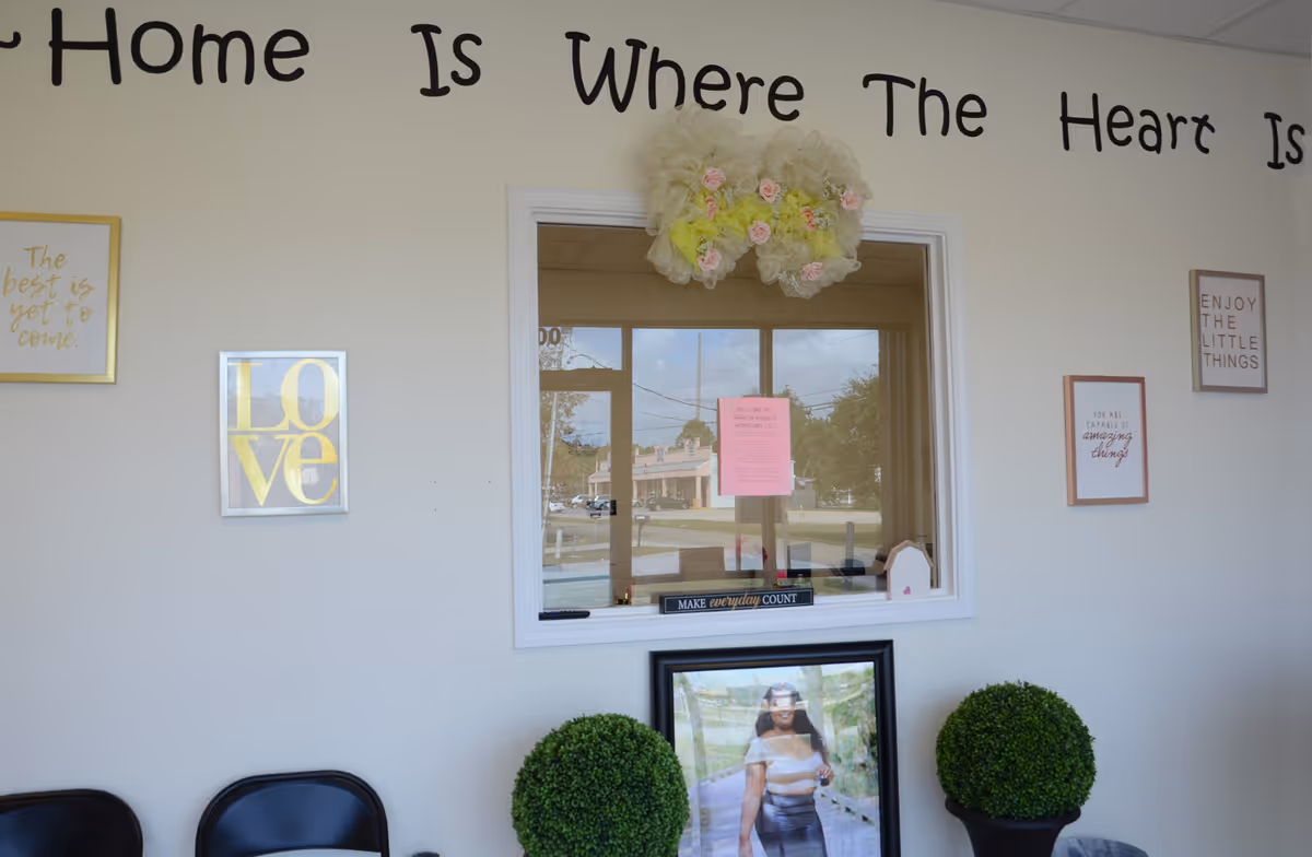 Interior wall with decor, window, framed quotes, and two potted topiary plants.