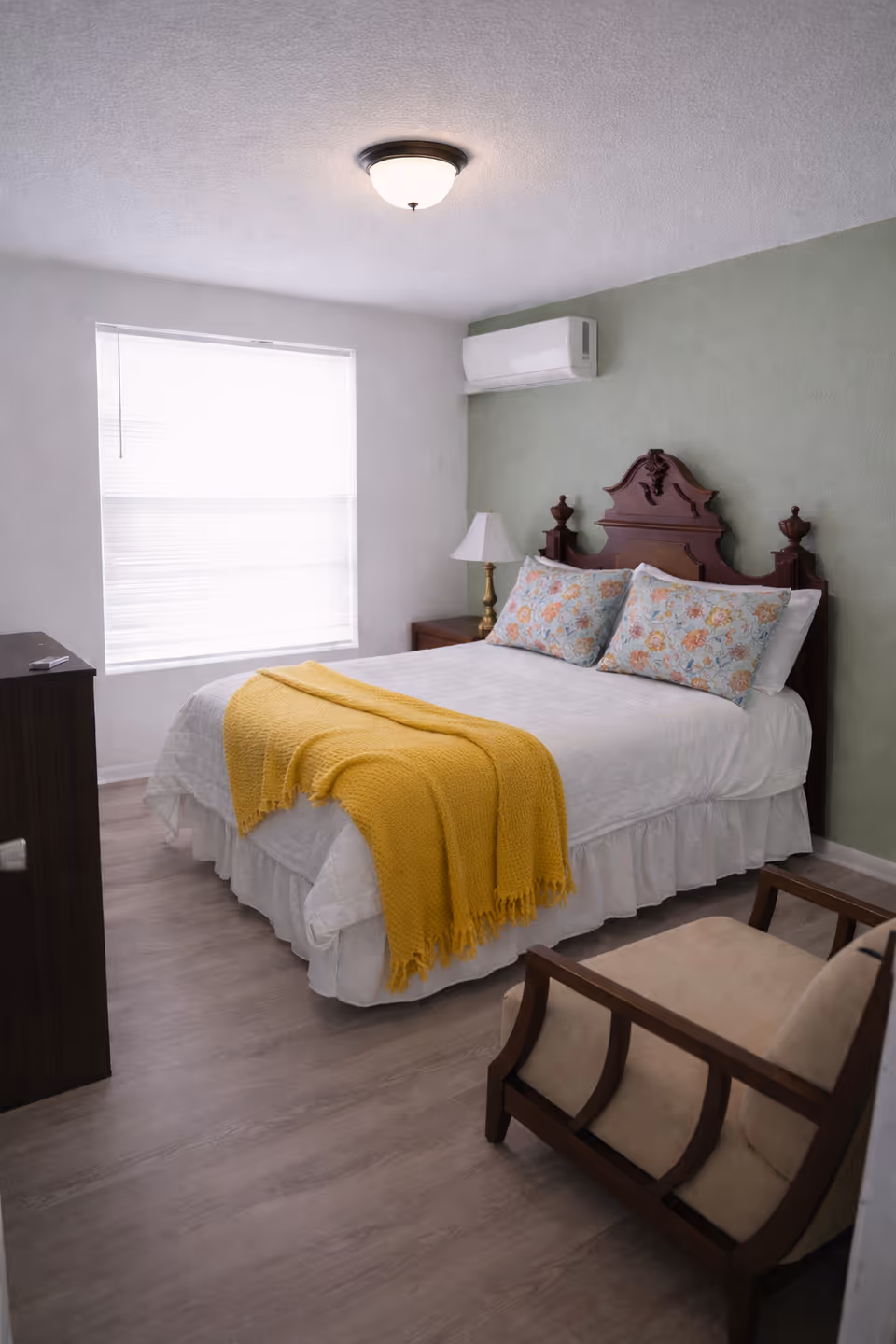 Cozy bedroom in a senior facility featuring a large bed, green wall, and yellow throw.
