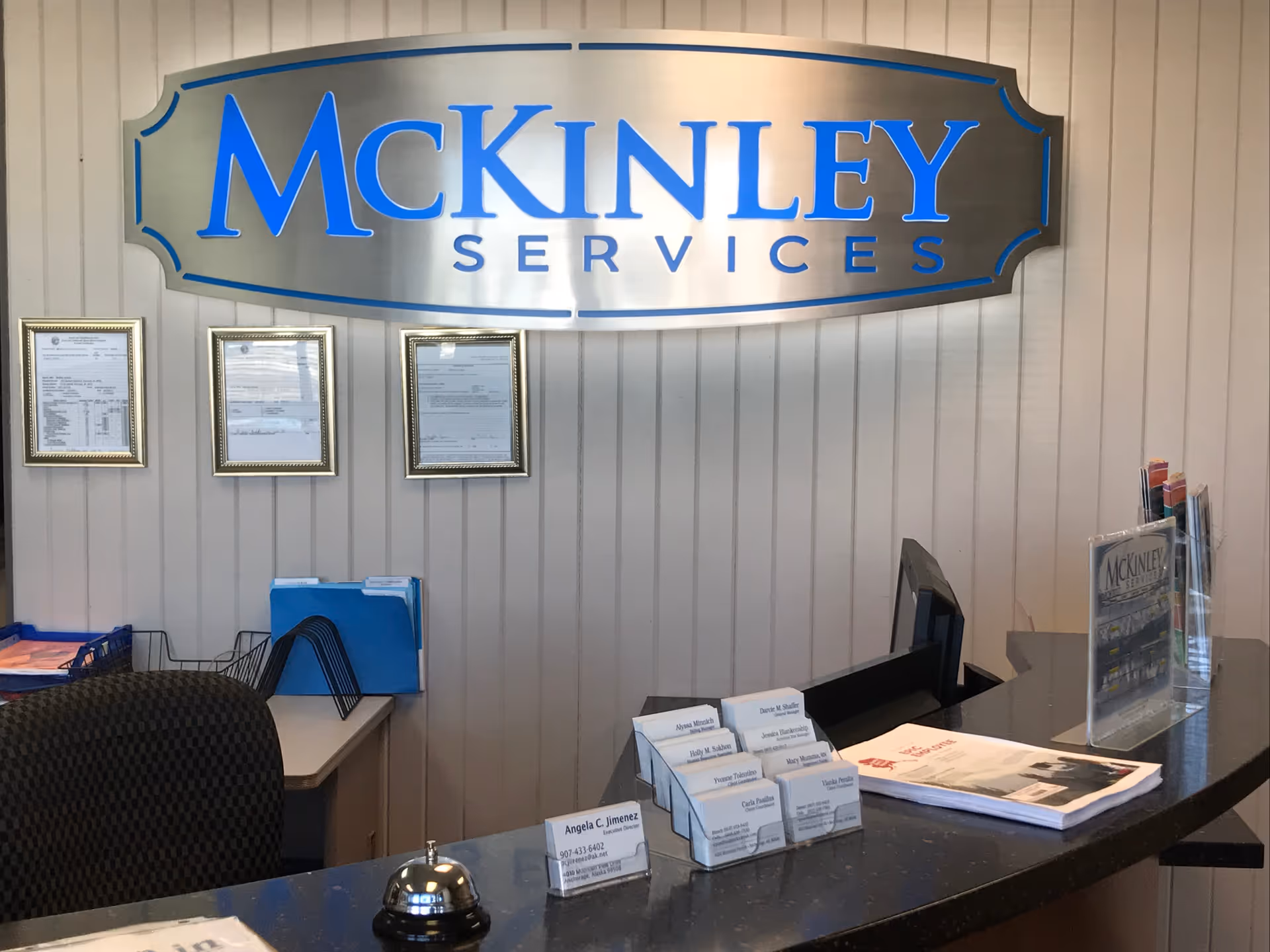 Reception desk with McKinley Services sign and framed documents on a paneled wall.
