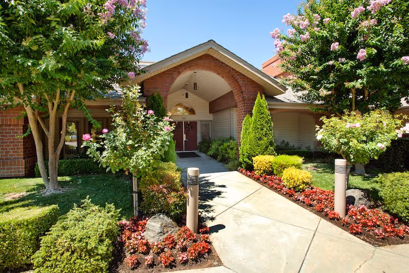 Sunny front entrance of Summerfield of Roseville with landscaped walkway and blooming trees.