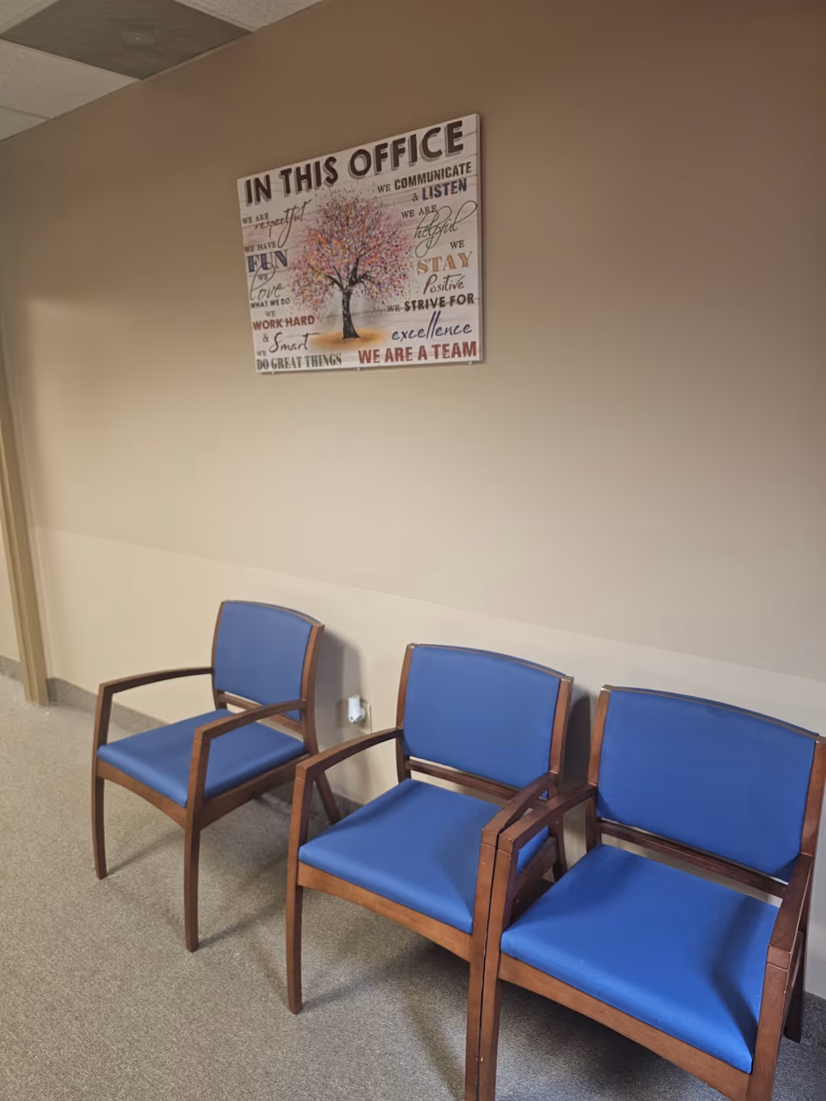 Blue cushioned chairs sit along a beige wall beneath a framed poster.