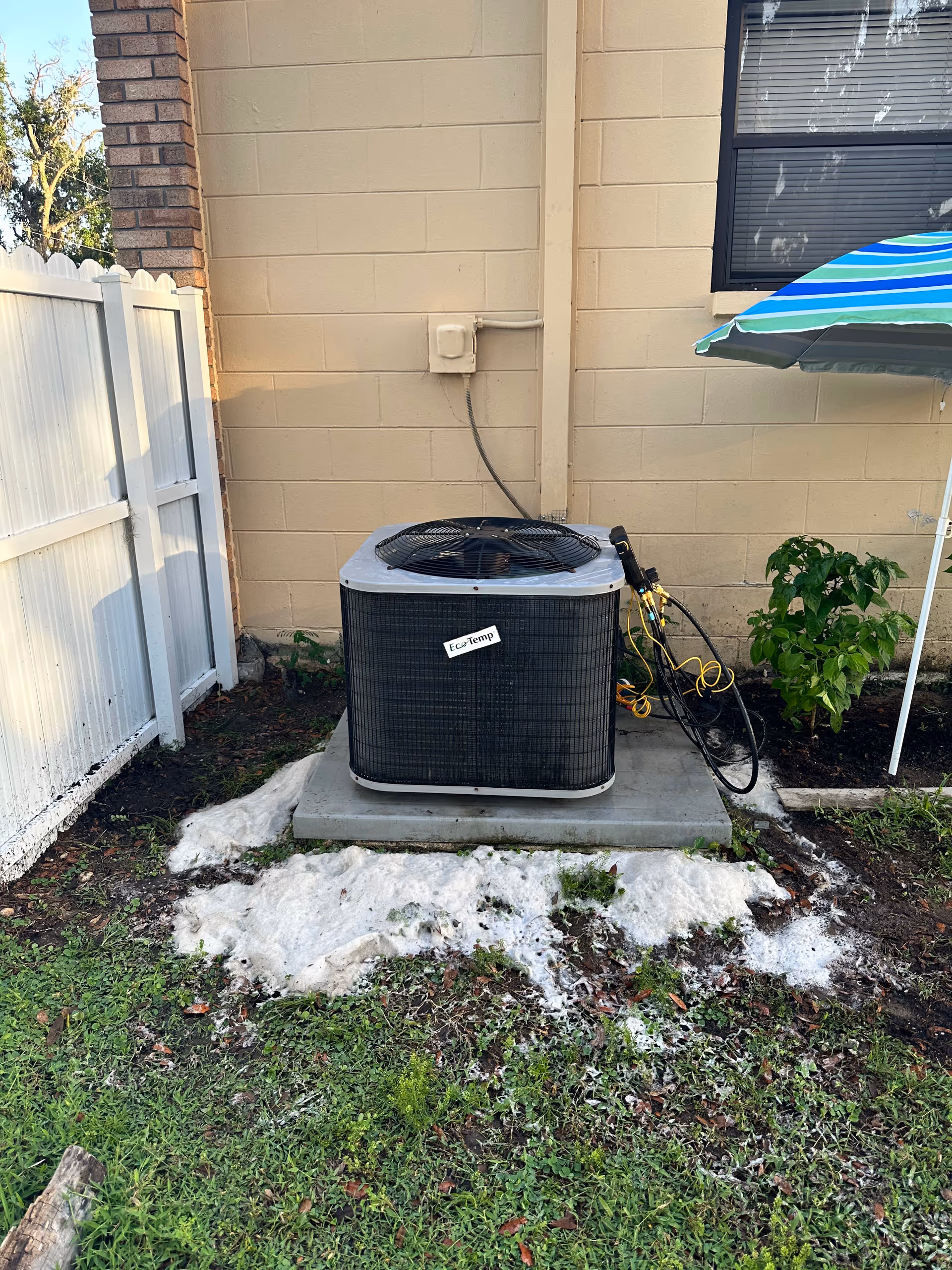 An outdoor air conditioner sits on a concrete pad beside a beige building wall.