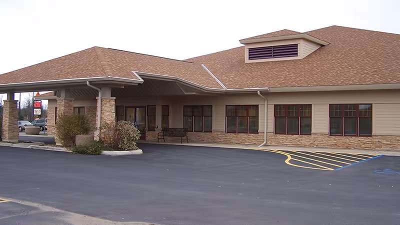 Exterior view of a senior care facility with a covered entrance and parking lot.