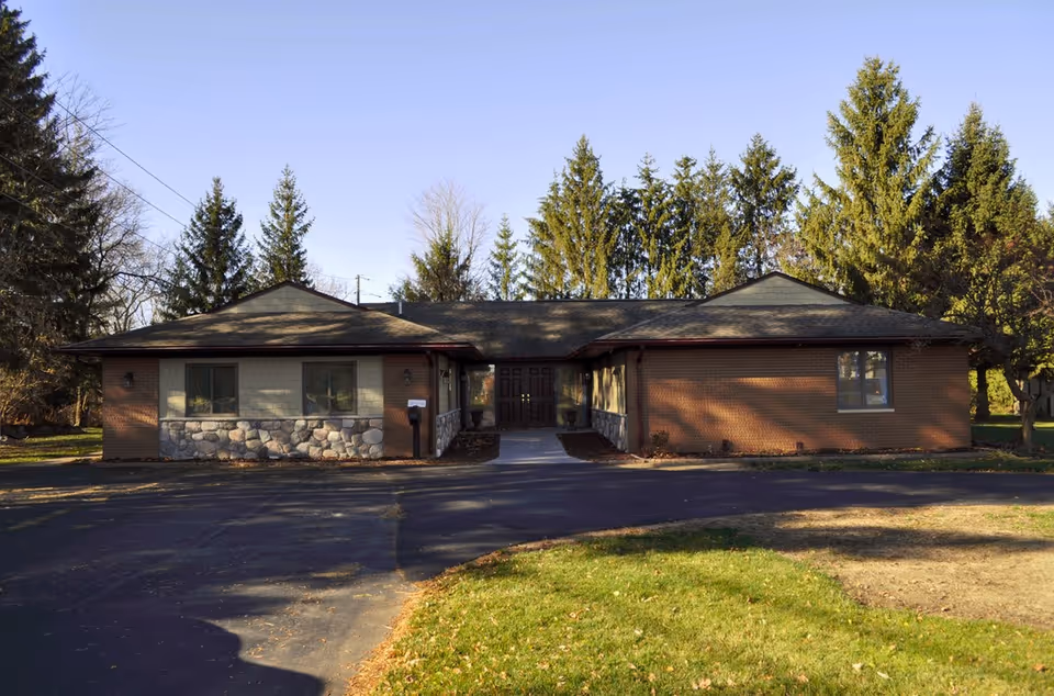 Single-story brick facility with stone accents, central entry, and surrounding trees.
