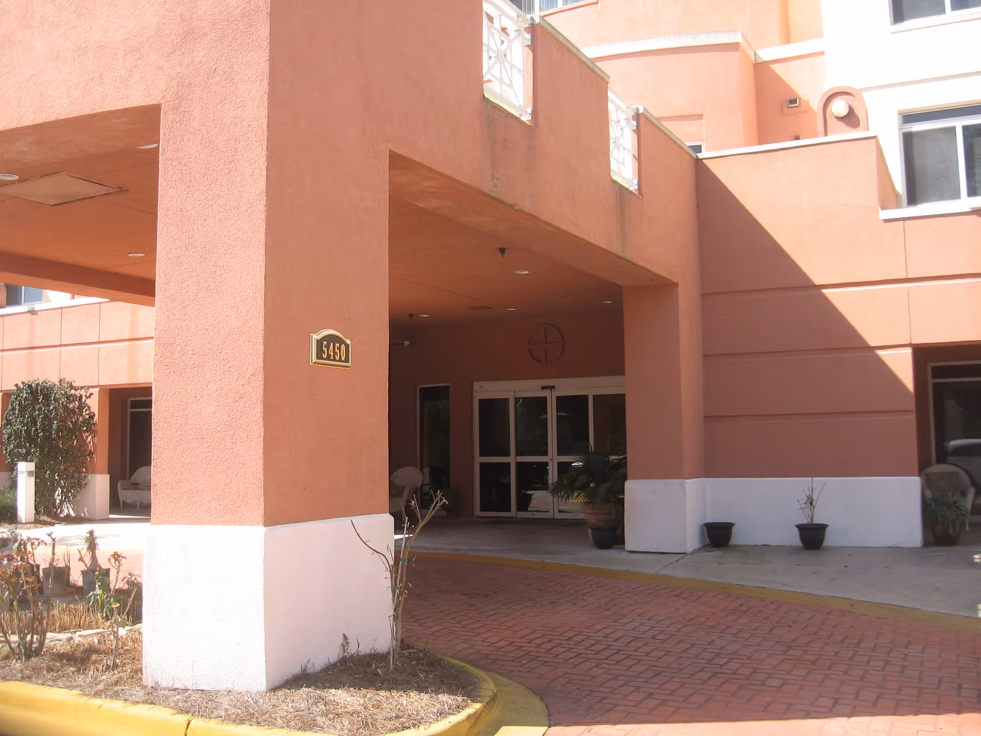 Exterior view of Buckingham South entrance with pink facade, pillars, and potted plants.