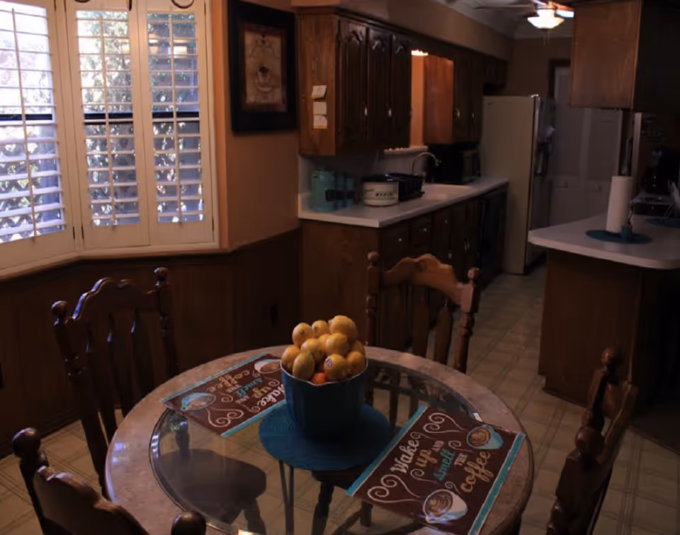 Dining area with a round glass table, fruit bowl, and wooden chairs.