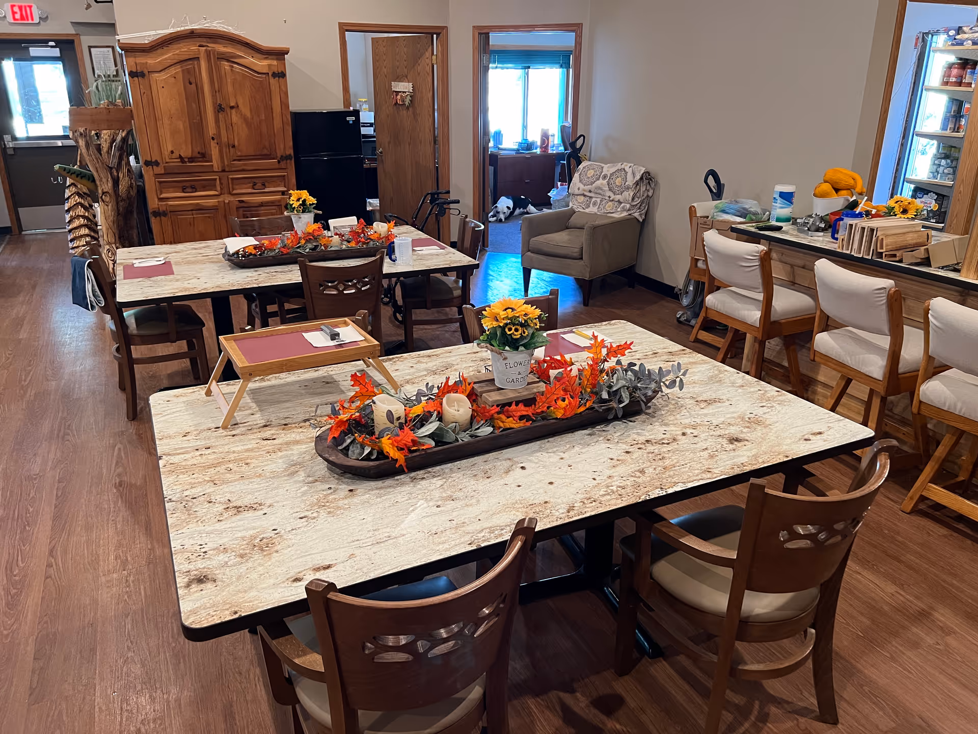 Dining room with multiple tables, chairs, and autumn decor in a senior living facility.