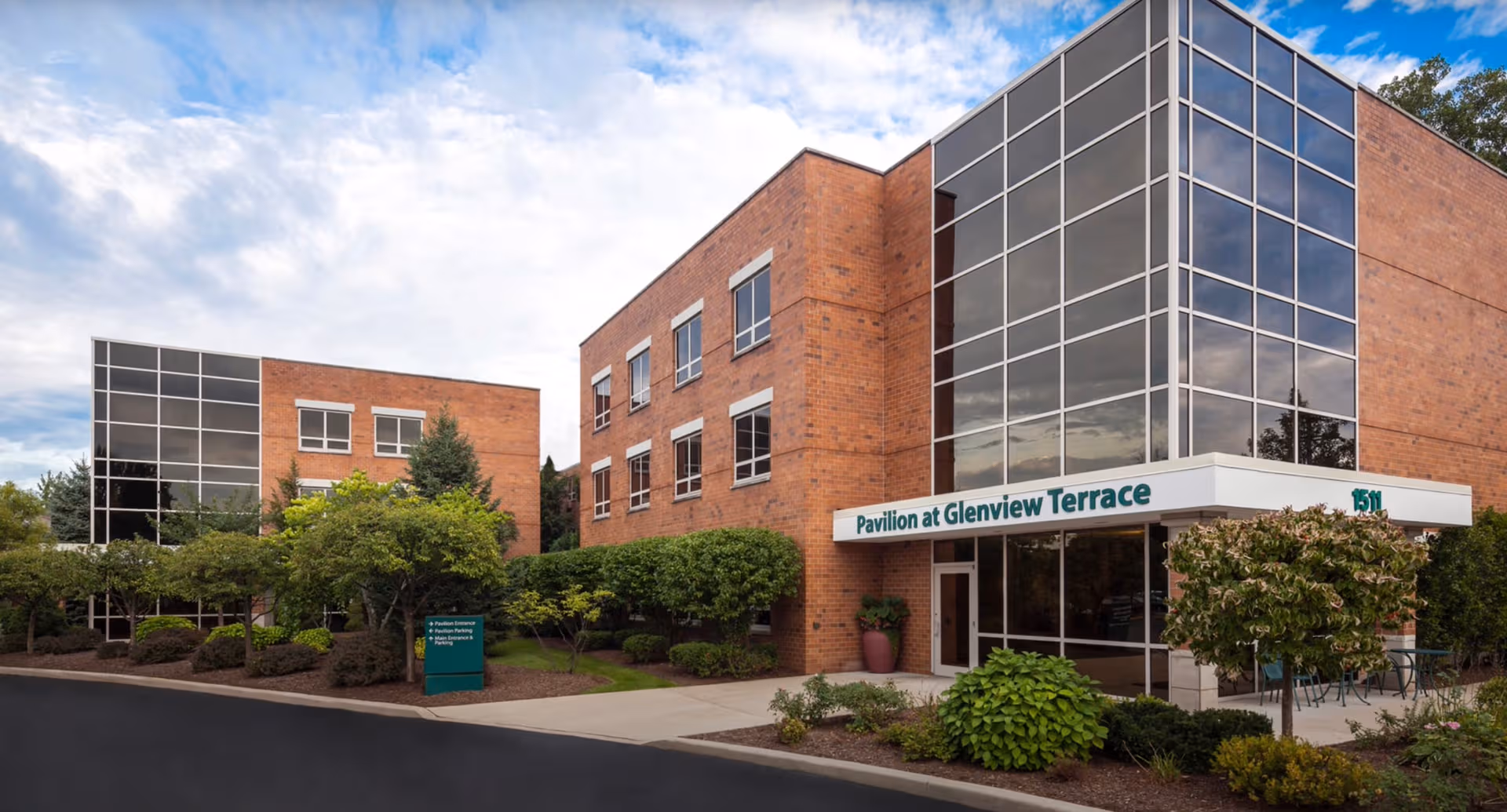 Exterior view of Pavilion at Glenview Terrace, brick building with glass entrance and landscaped surroundings.