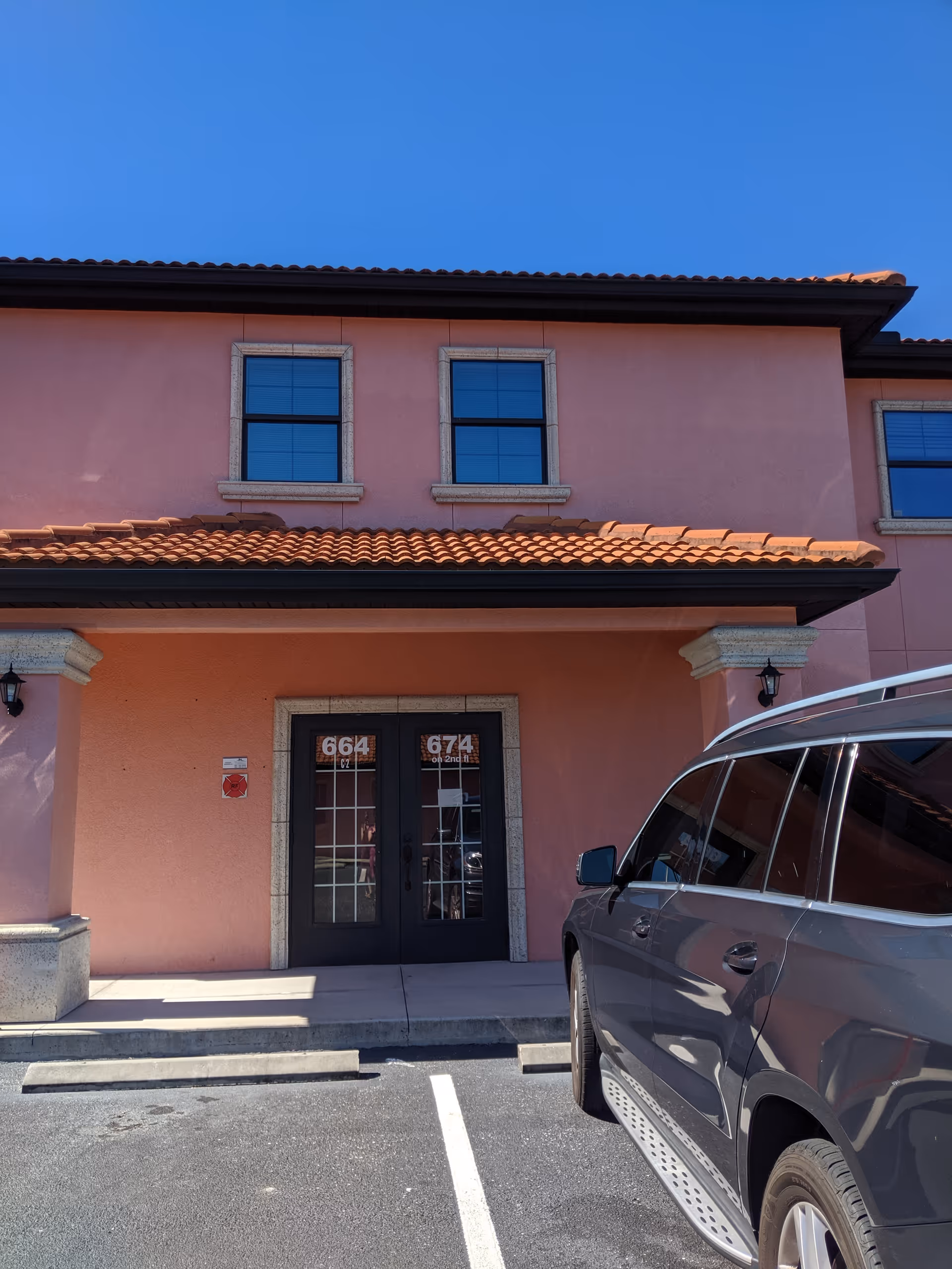 Pink stucco building front with black doors, tiled roof, and a parked SUV.
