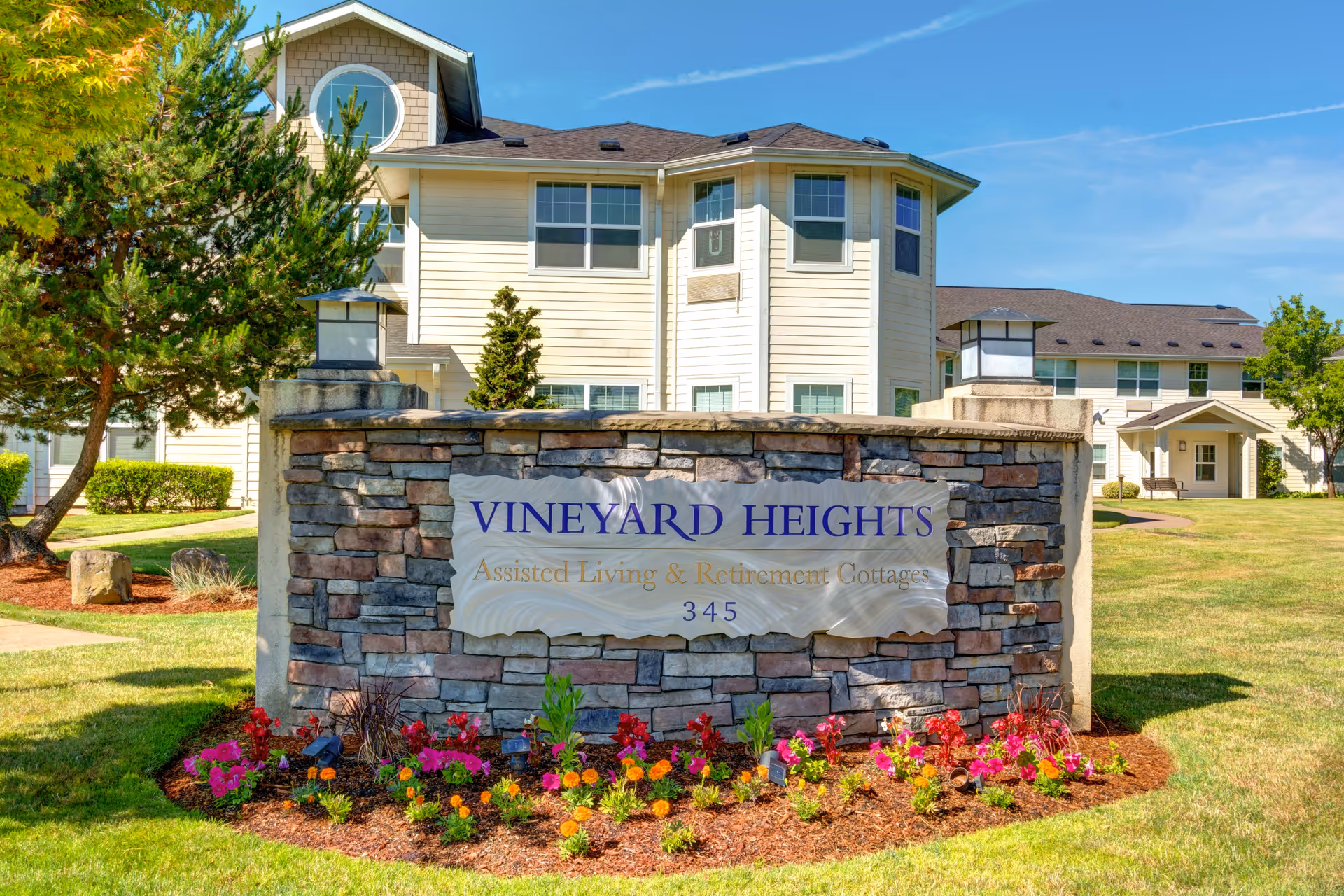 Stone sign reads Vineyard Heights with a flowering bed and a modern building in background.