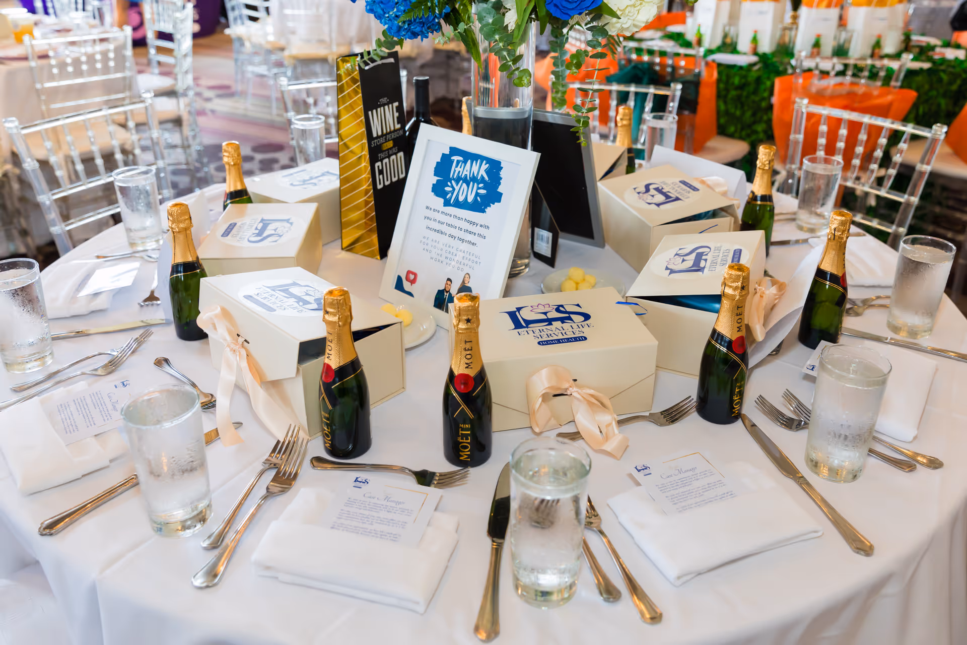 Round banquet table with champagne bottles, gift boxes, and a Thank You card at an event.