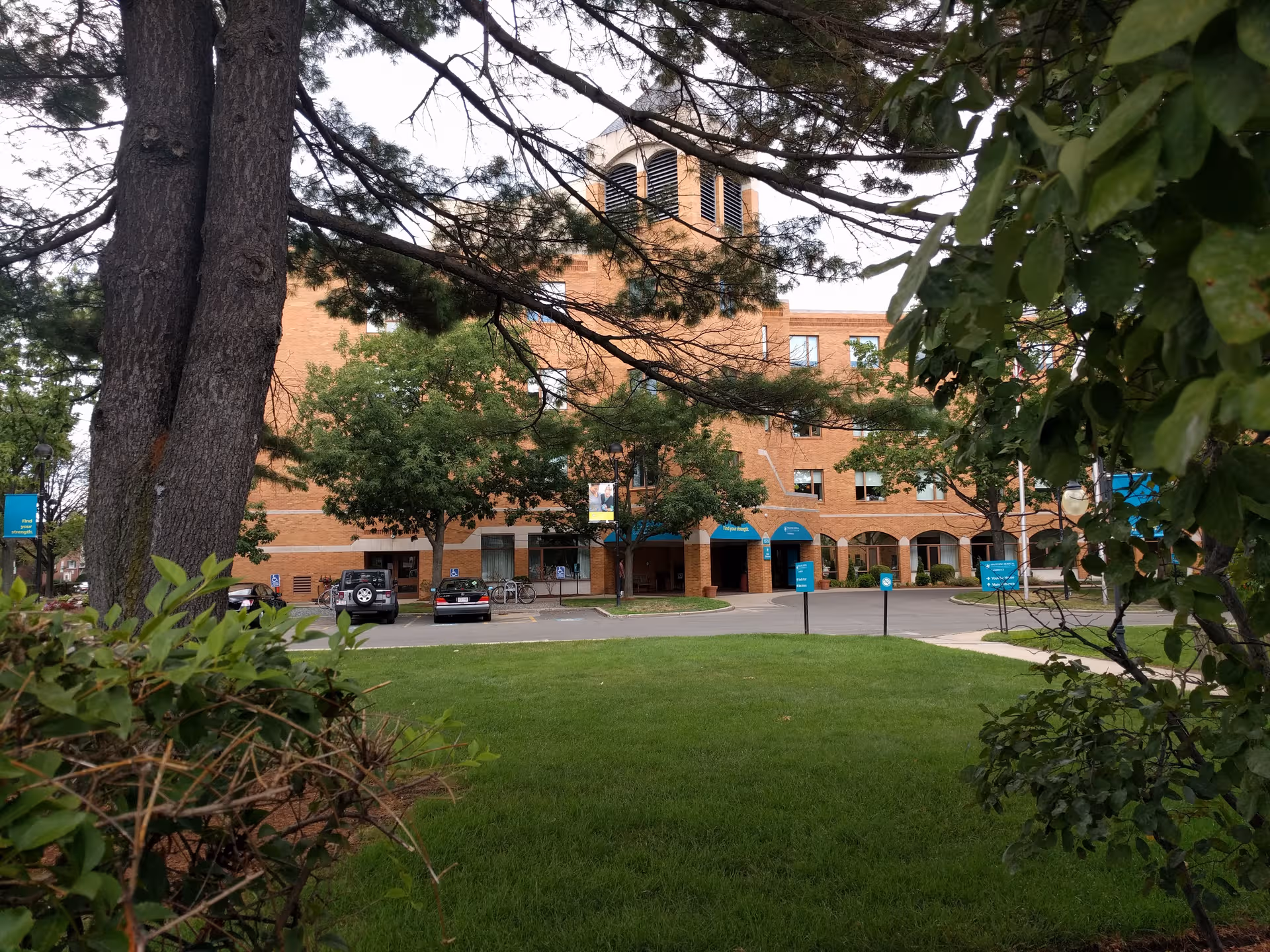 Brick senior living building with blue awnings, arches, and surrounding greenery.