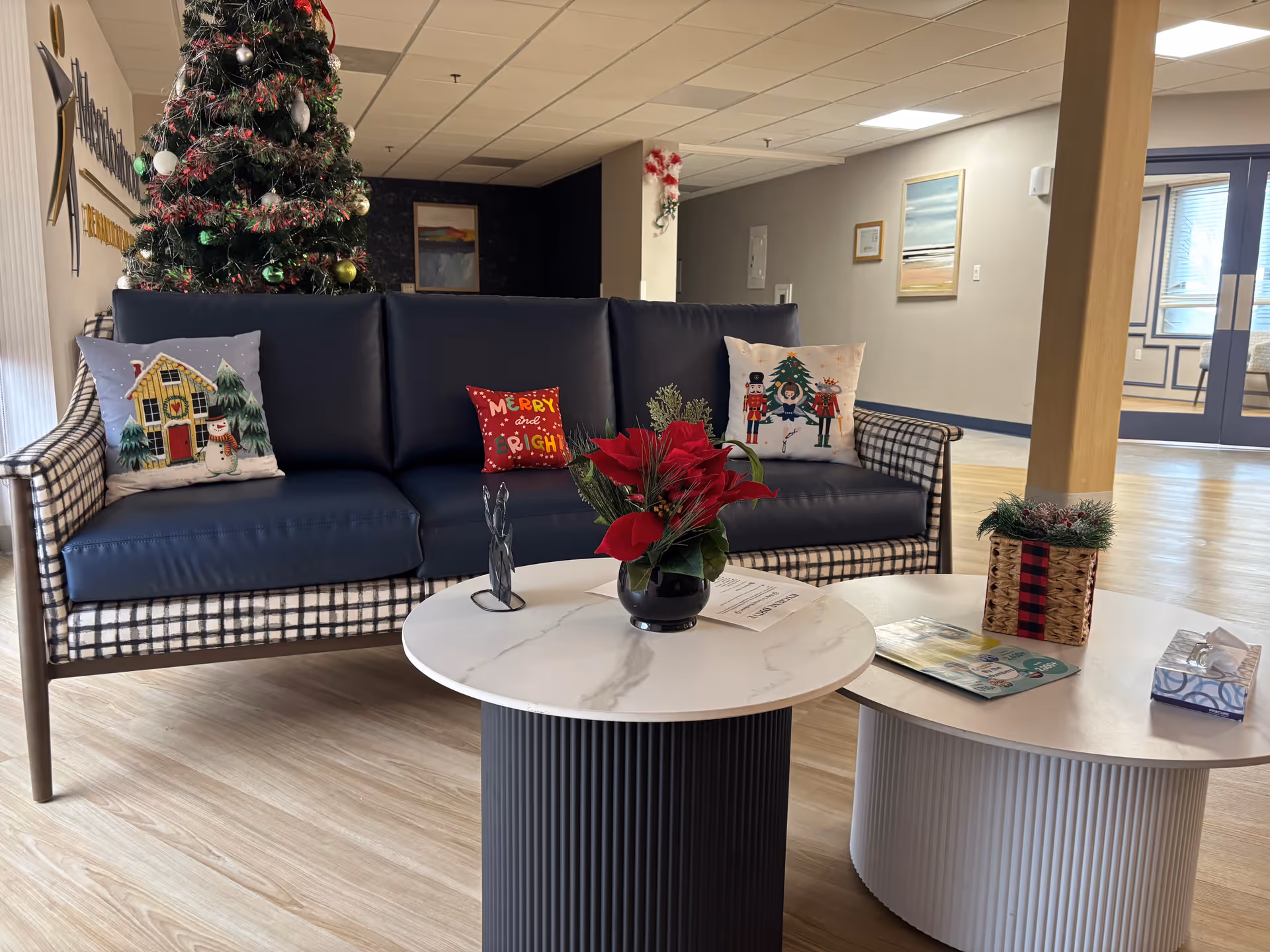 Cozy hospital lobby lounge with a checkered sofa, Christmas tree, and two round marble coffee tables.