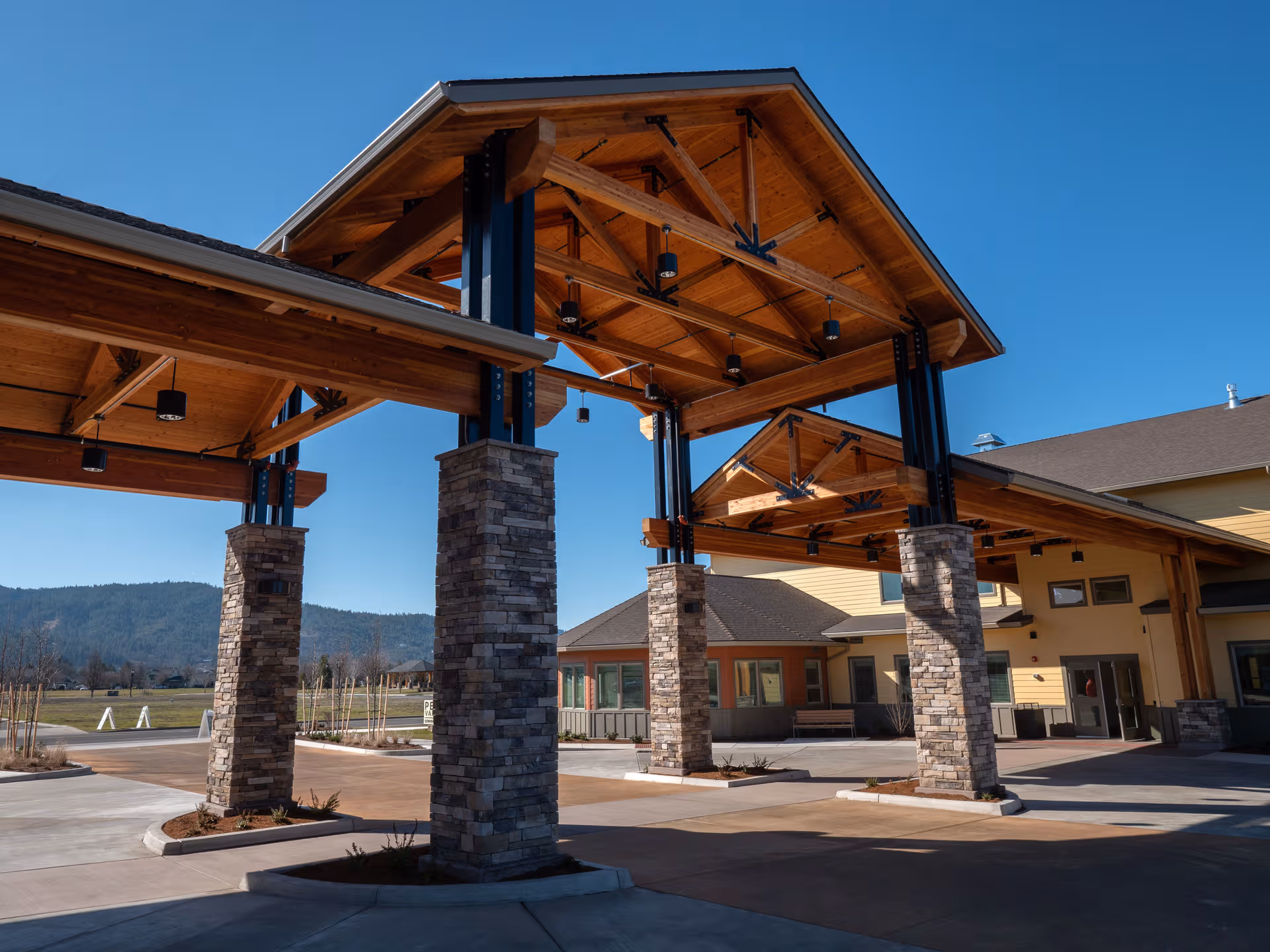 Wood and stone entrance canopy with large pillars leads to Pear Valley Senior Living building.