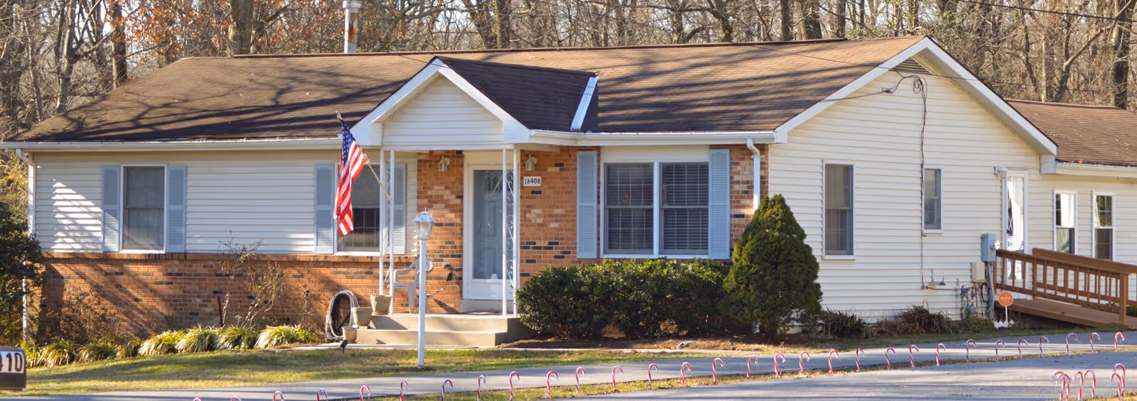 Front exterior of a single-story senior living facility with flag and shrubs.
