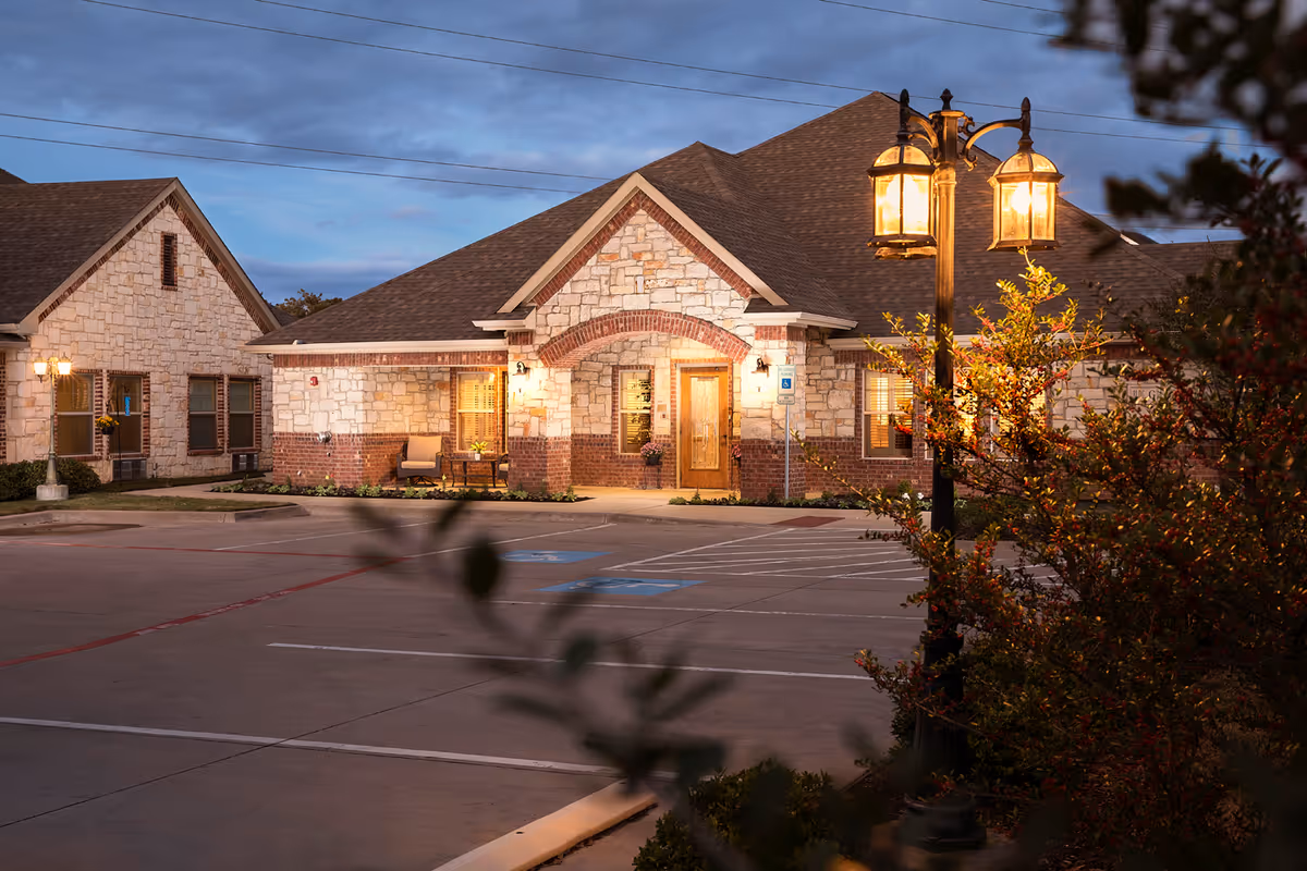 Exterior view of Mustang Creek Estates Keller, a stone-brick senior living facility at dusk.