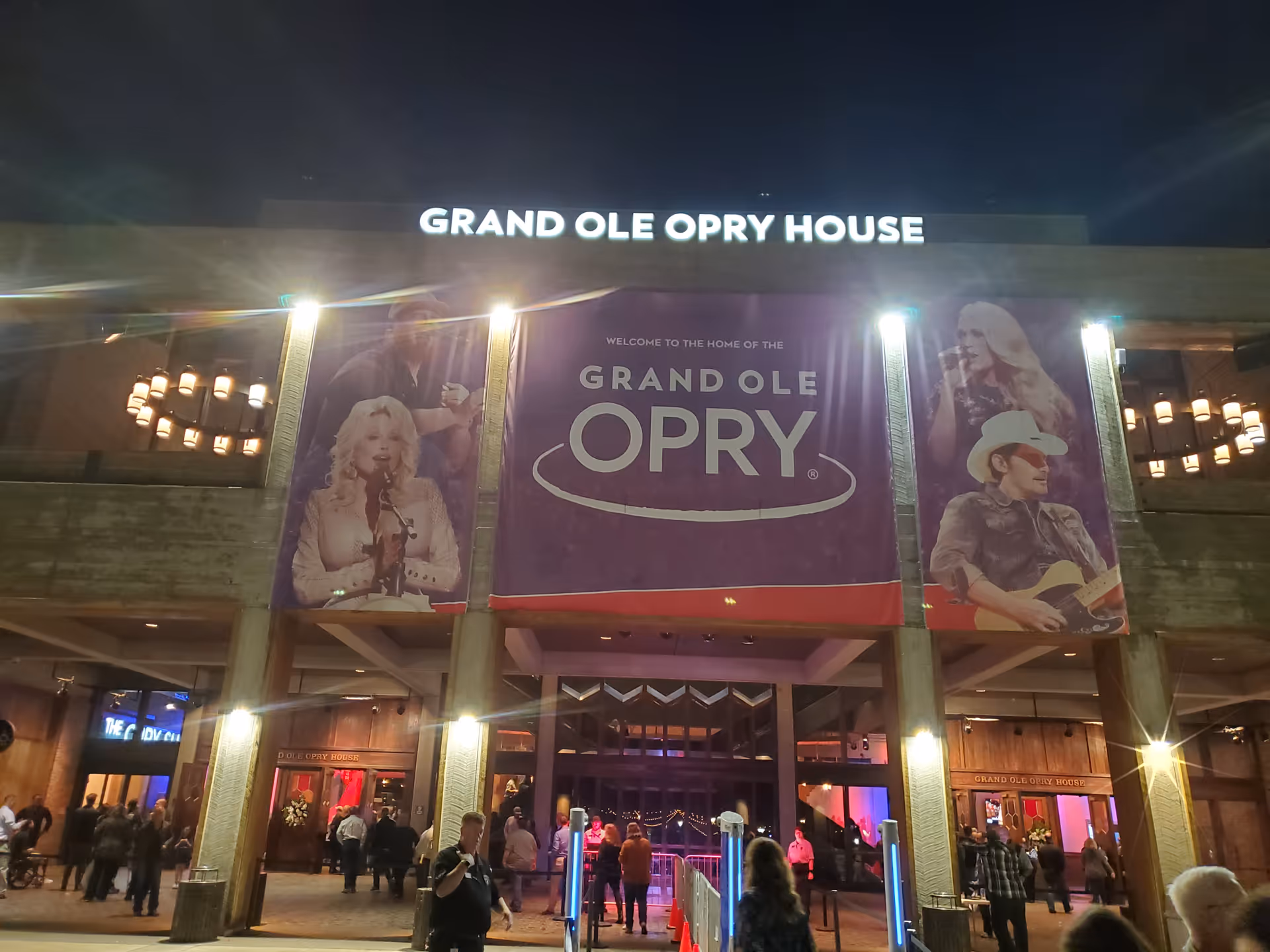Night exterior of Grand Ole Opry House with large banners and people outside.