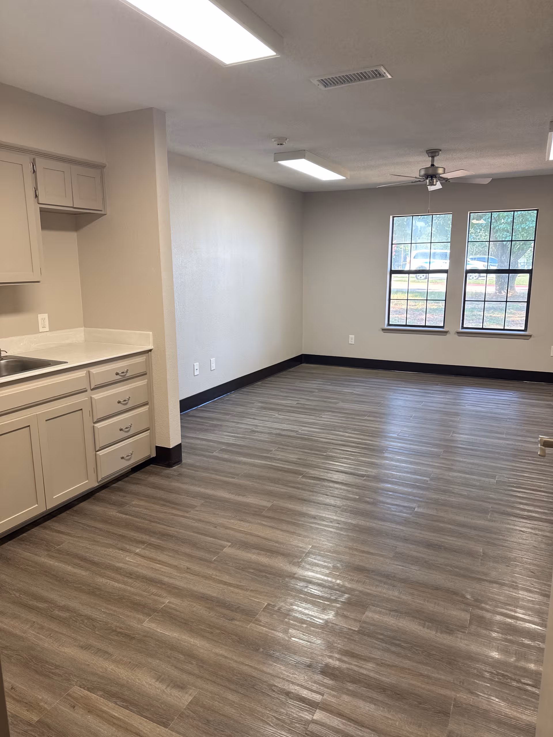 Open living area with kitchenette, large windows, and a ceiling fan.