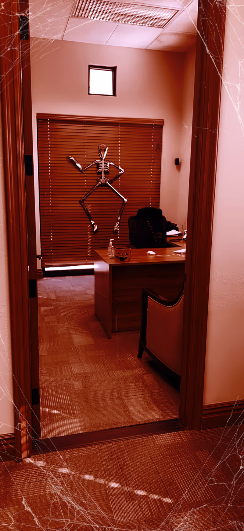 Interior office area in a senior living facility with a desk, blinds, and a skeleton decoration.