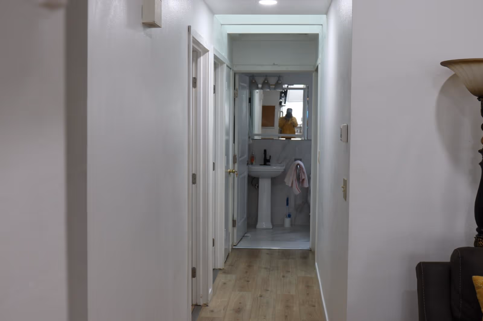 Narrow residential hallway leading to a small bathroom with pedestal sink and mirror