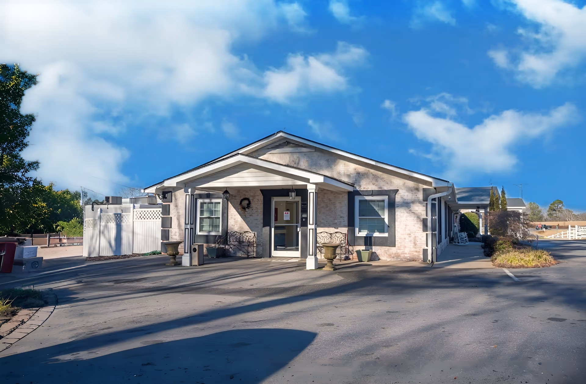Front view of Alberta House entrance with seating outside and a driveway under a blue sky.
