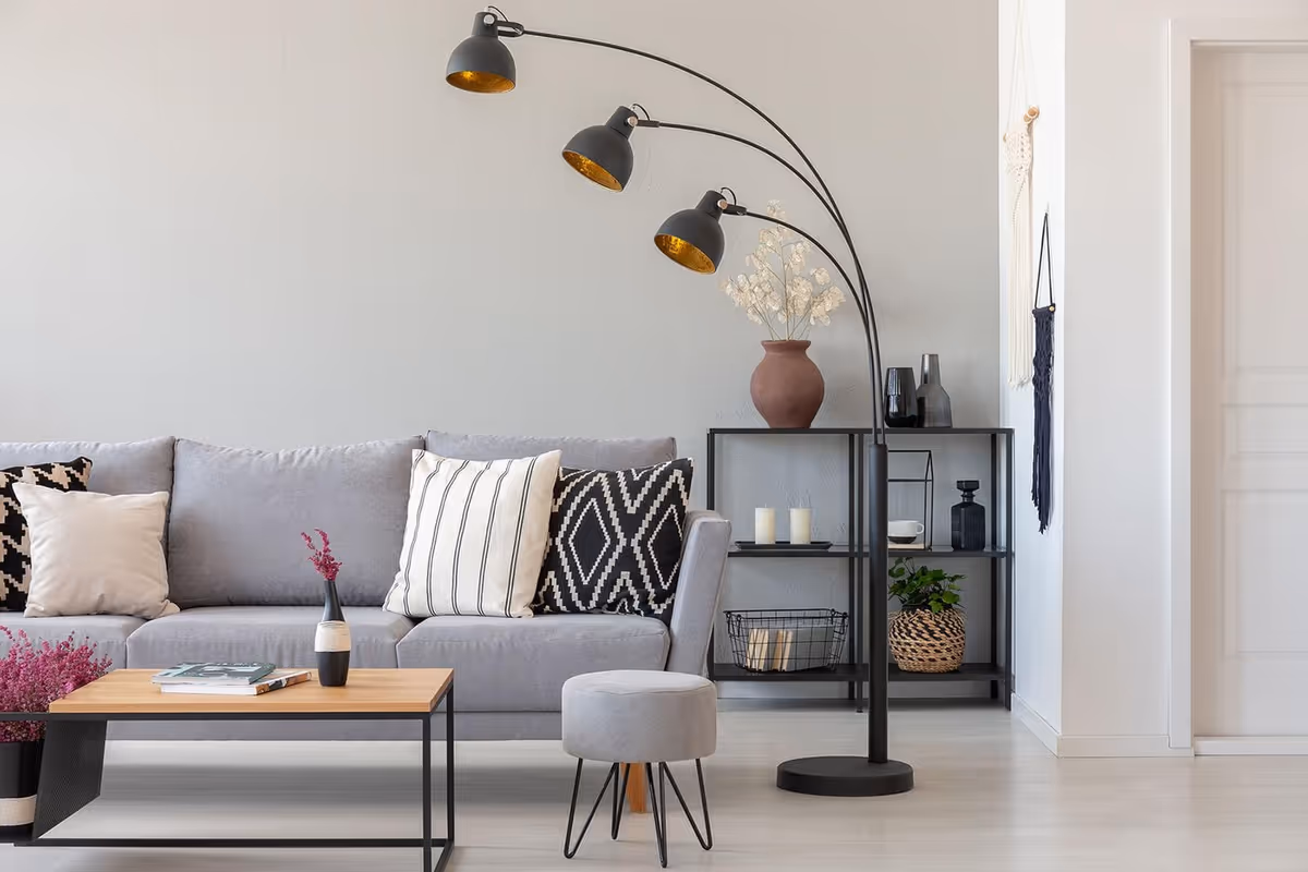 Modern living room with a gray sofa, patterned throw pillows, an arc floor lamp, coffee table and shelving with decor.