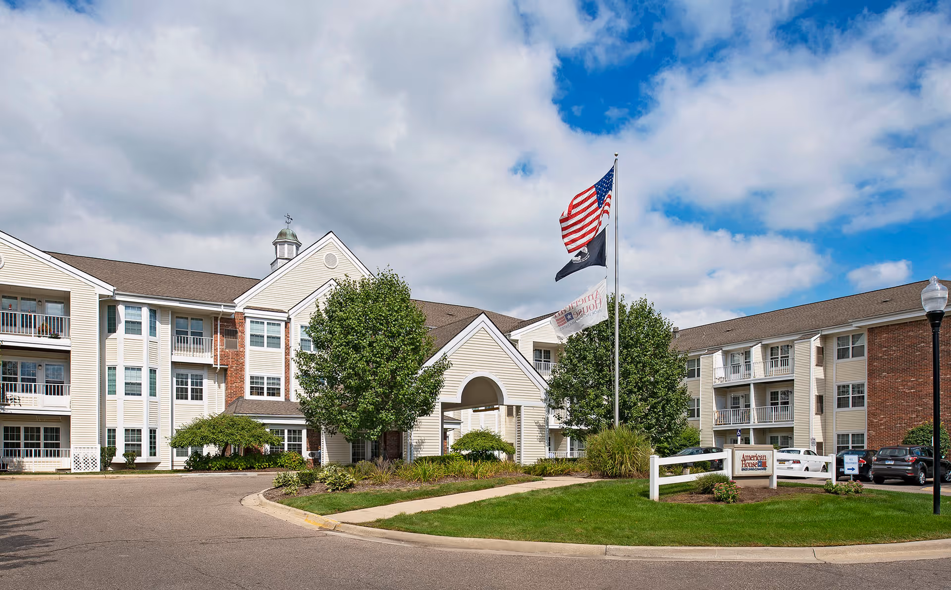 Exterior view of Baldwin House Senior Living Hazel Park with flags and entryway.