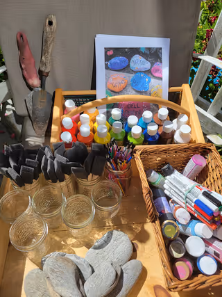 Outdoor craft station with paints, brushes, jars, and decorative stones on a wooden table.